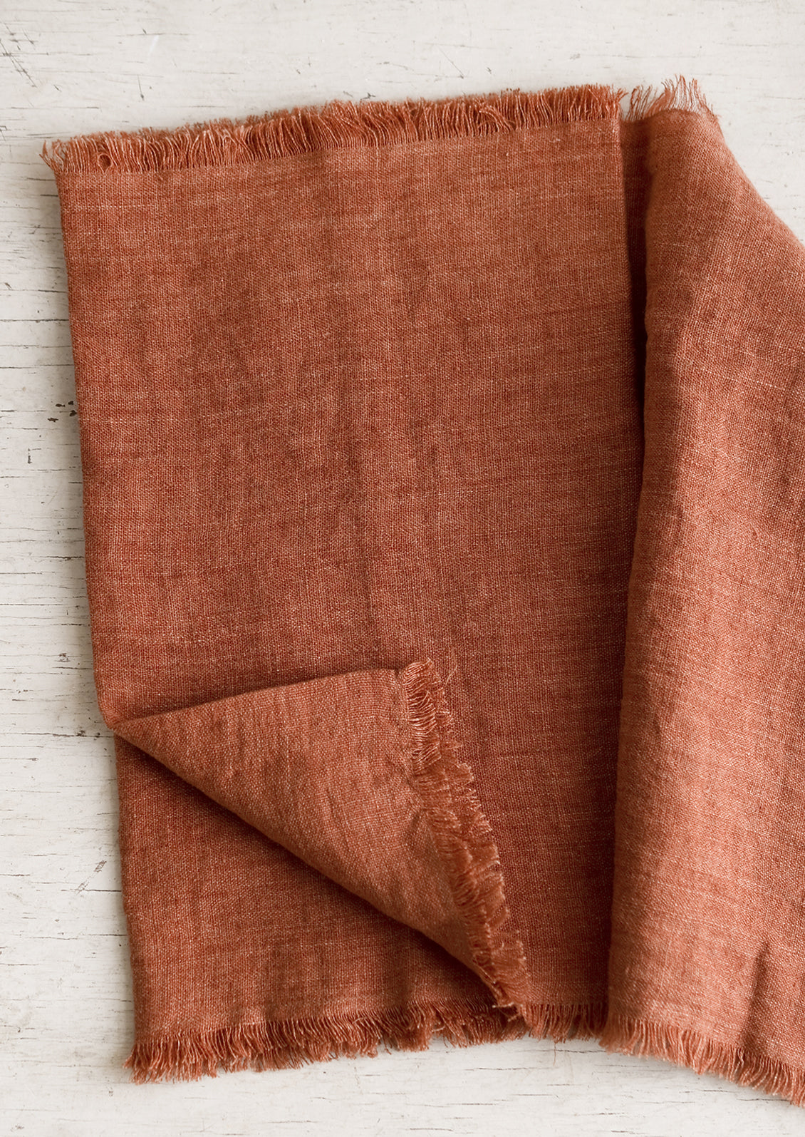 A linen table runner with frayed edges in paprika.