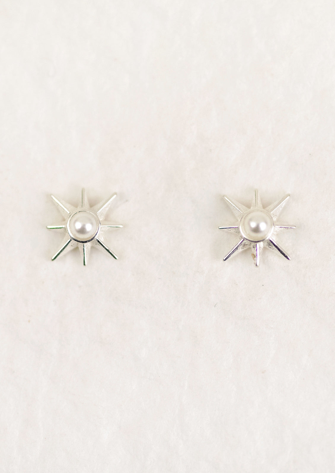 A pair of sterling silver starburst earrings with a pearl center.