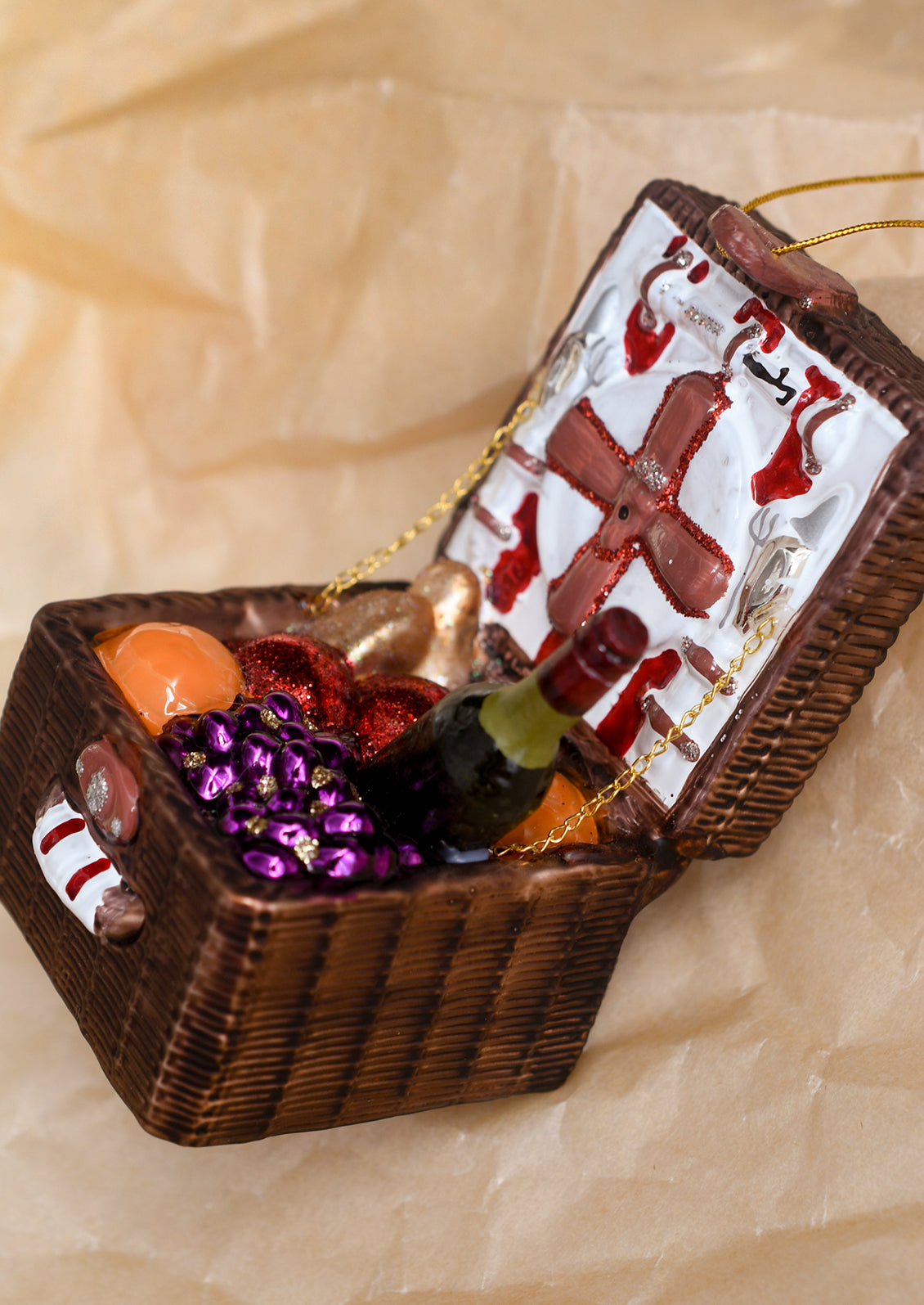 A glass ornament depicting an open picnic basket with wine, bread and fruit.
