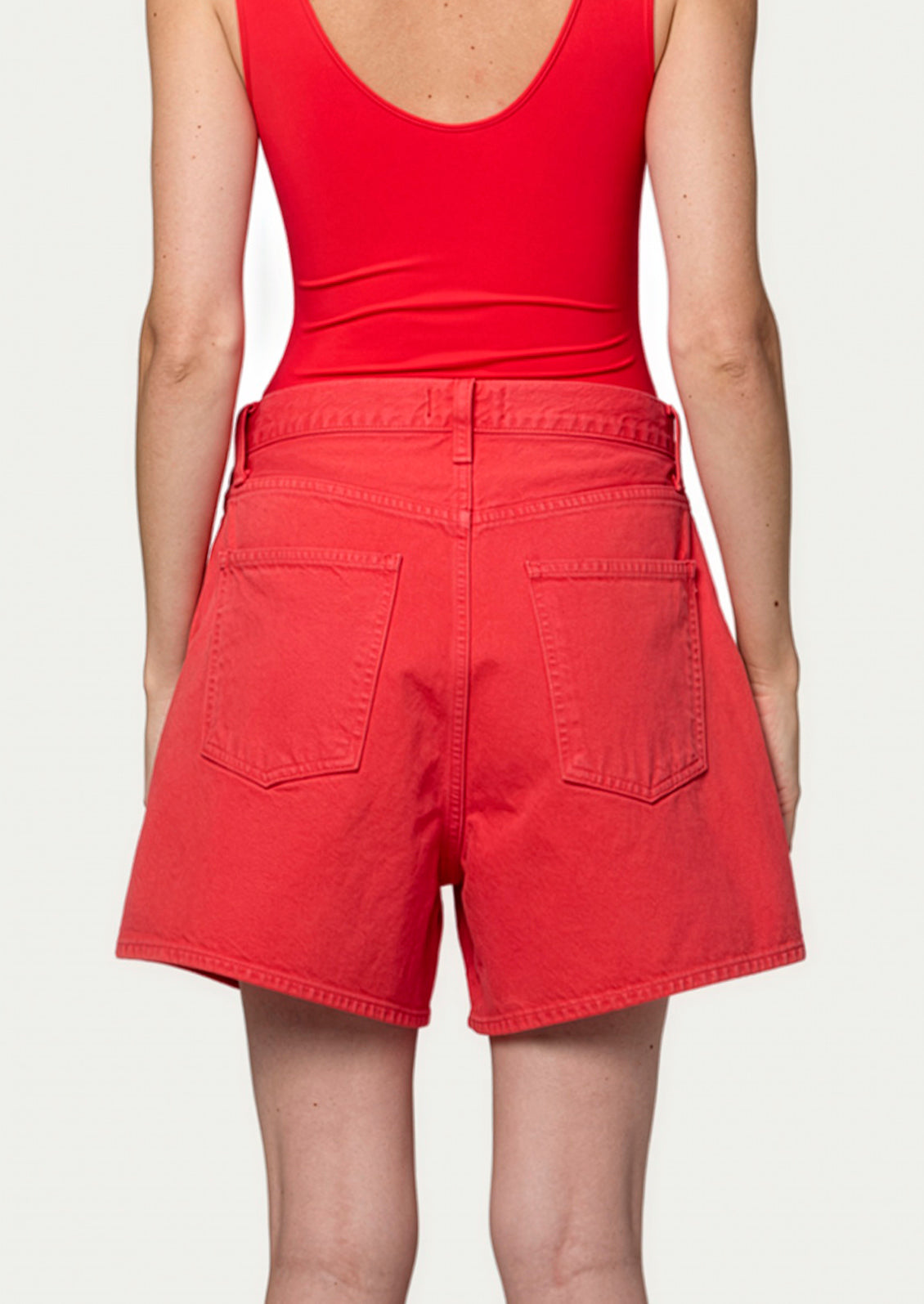 A person wearing a pair of pleated a-line shorts in red.