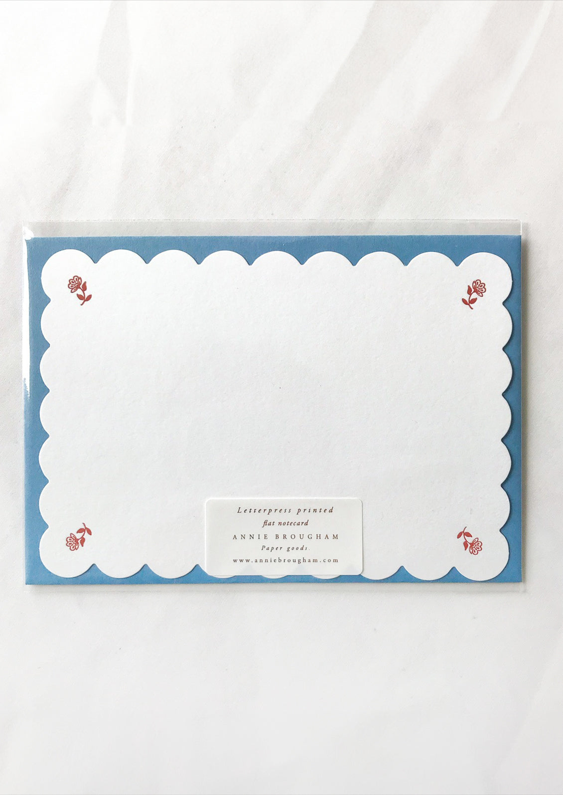 A scalloped white notecard with red floral at corners and blue envelope.