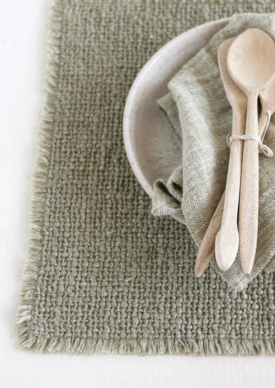 A sage green placemat with fringe edges.