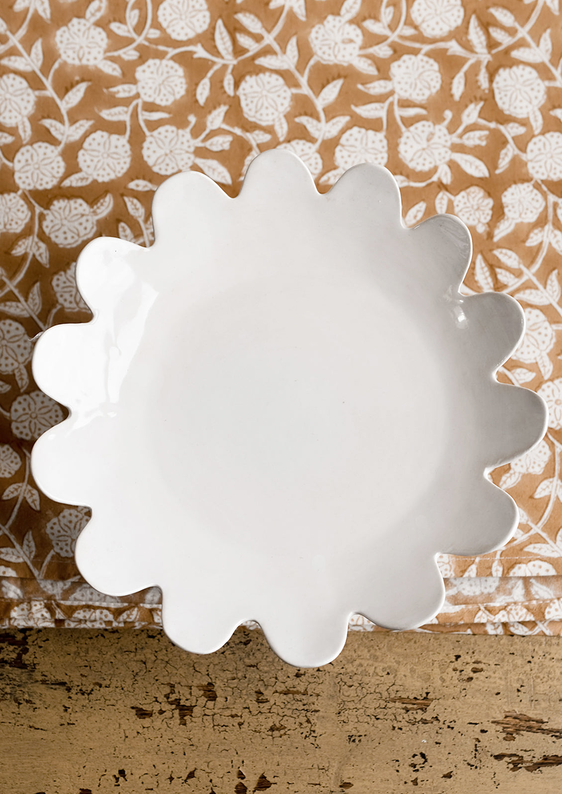 A pedestal riser in gloss white ceramic with scalloped plate shape.