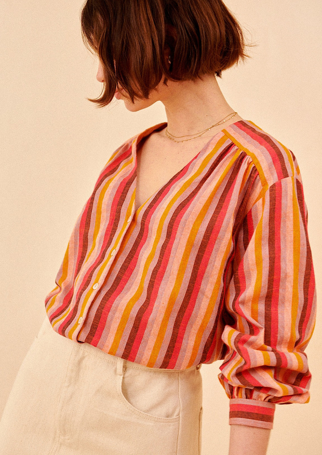 A woman wearing a v-neck, button front blouse in warm color stripe pattern.