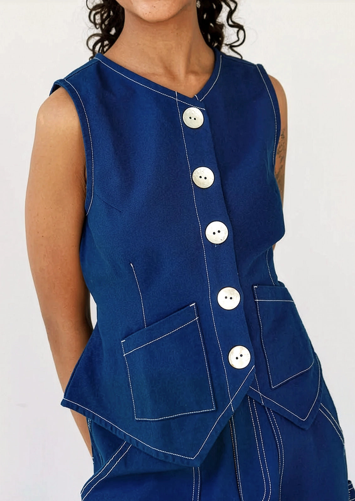 A person wearing a navy sleeveless top with large white shell buttons.