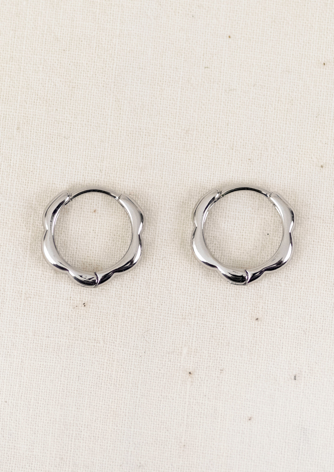 A pair of small silver hoop earrings with a scallop edge design