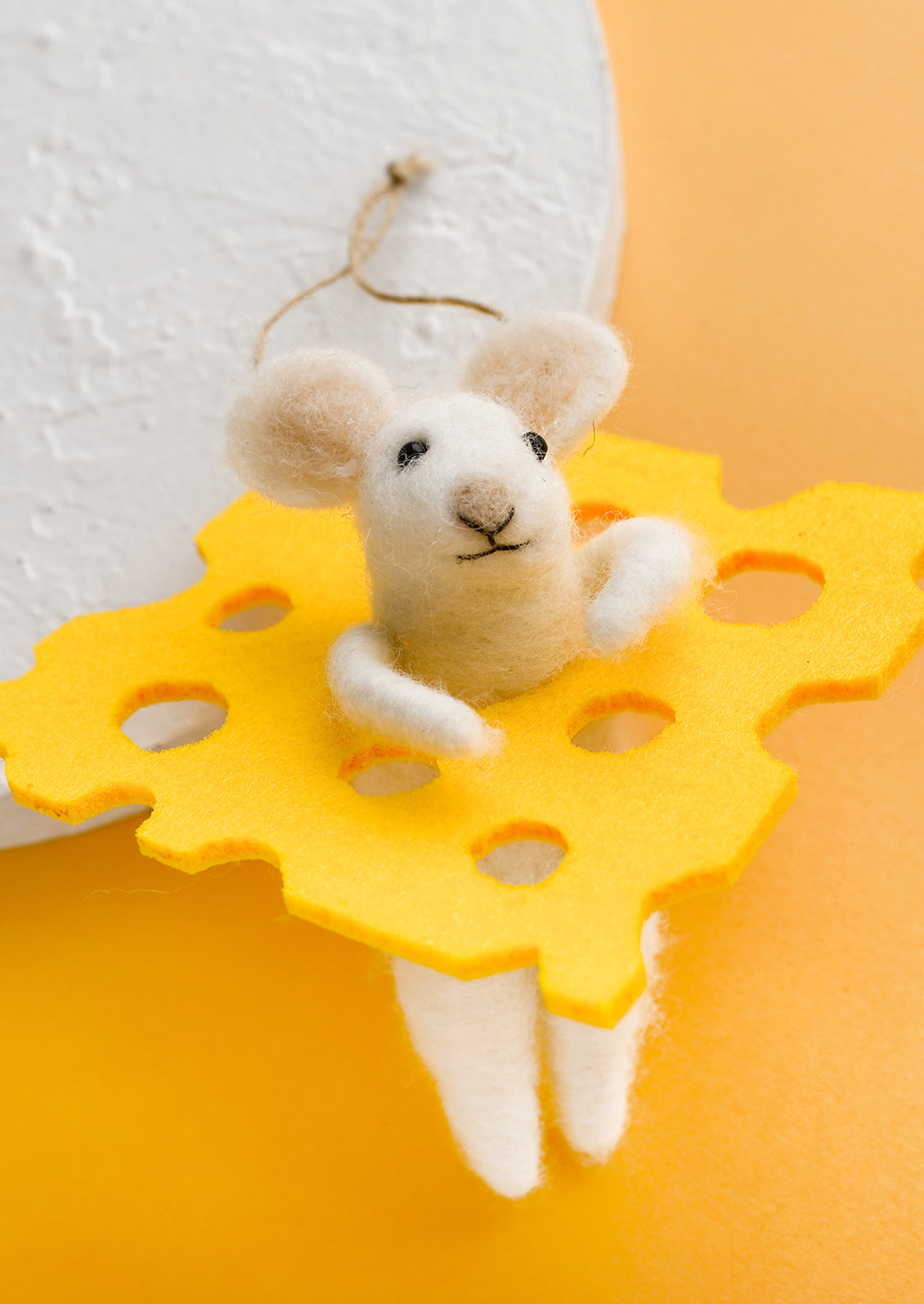 A felted wool ornament of white mouse and slice of cheese.