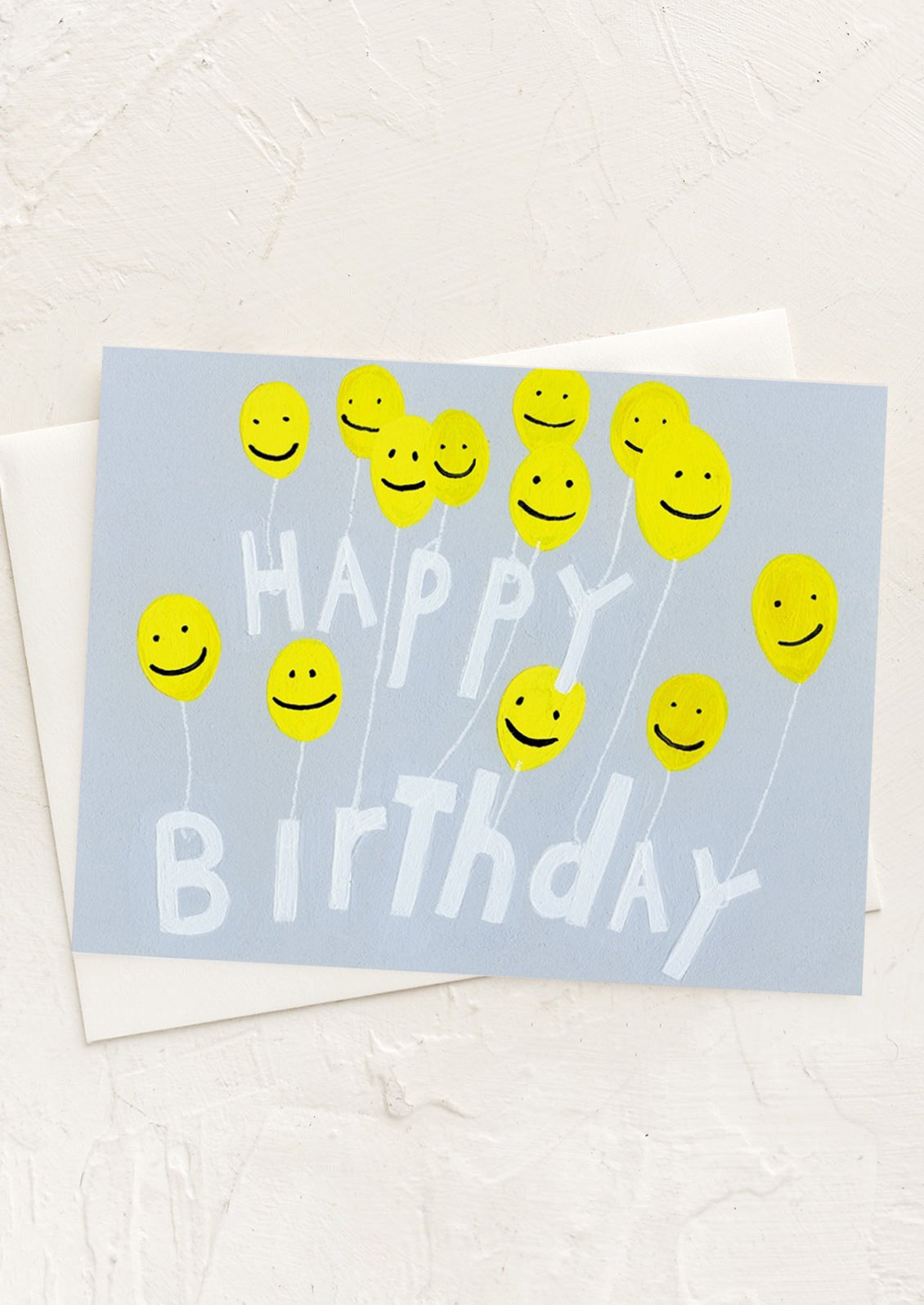 A greeting card with illustration of smiley face yellow balloons holding text reading "Happy Birthday".