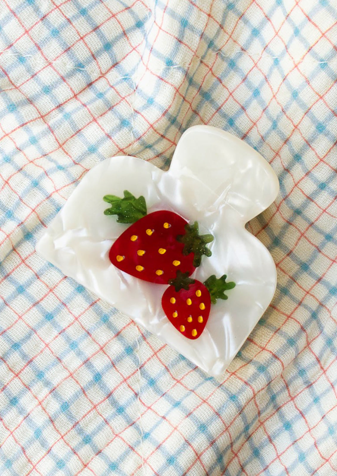 A pearl white hair clip with red strawberry.