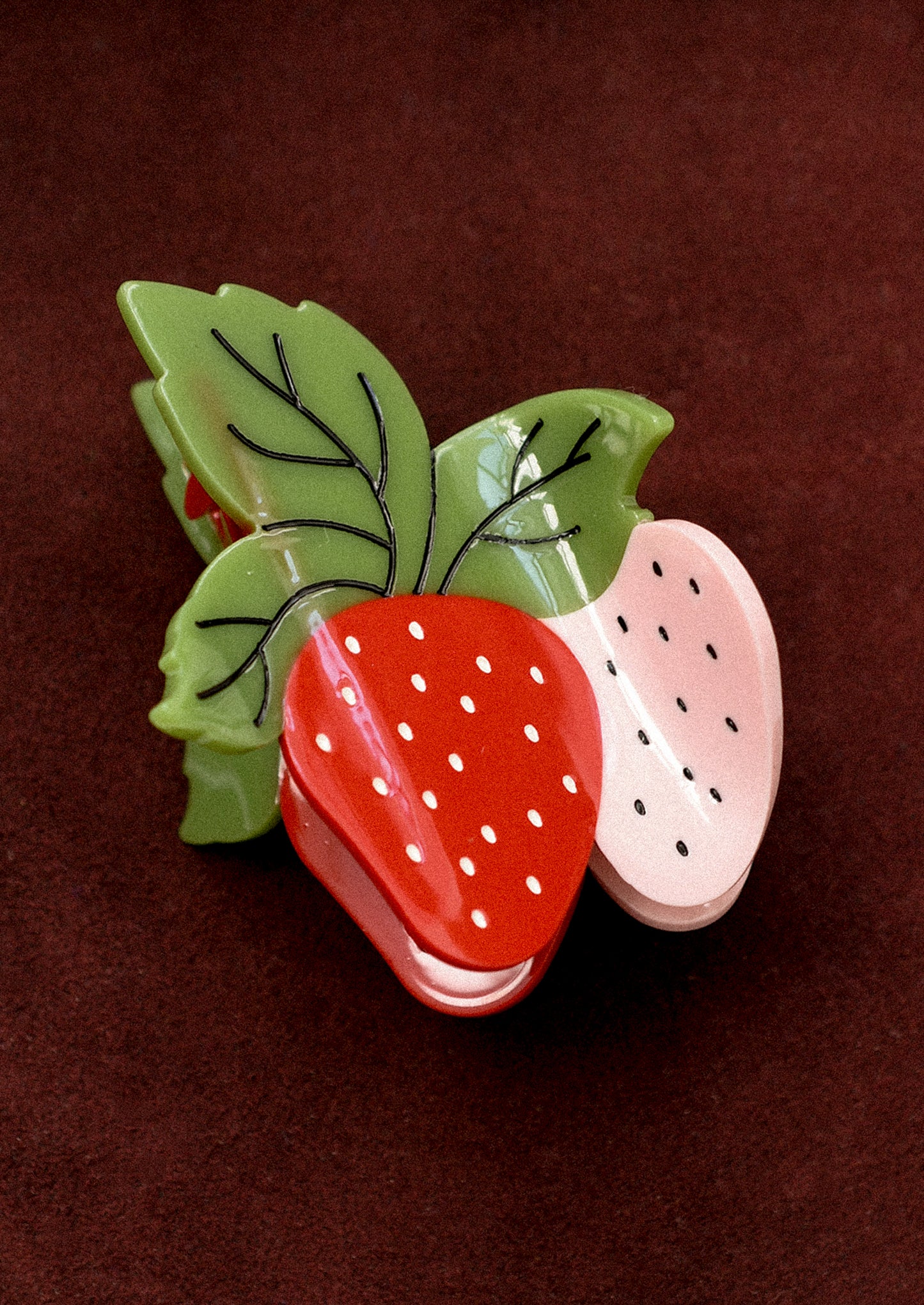 A strawberry shaped hair claw in red and pink with green leaves.