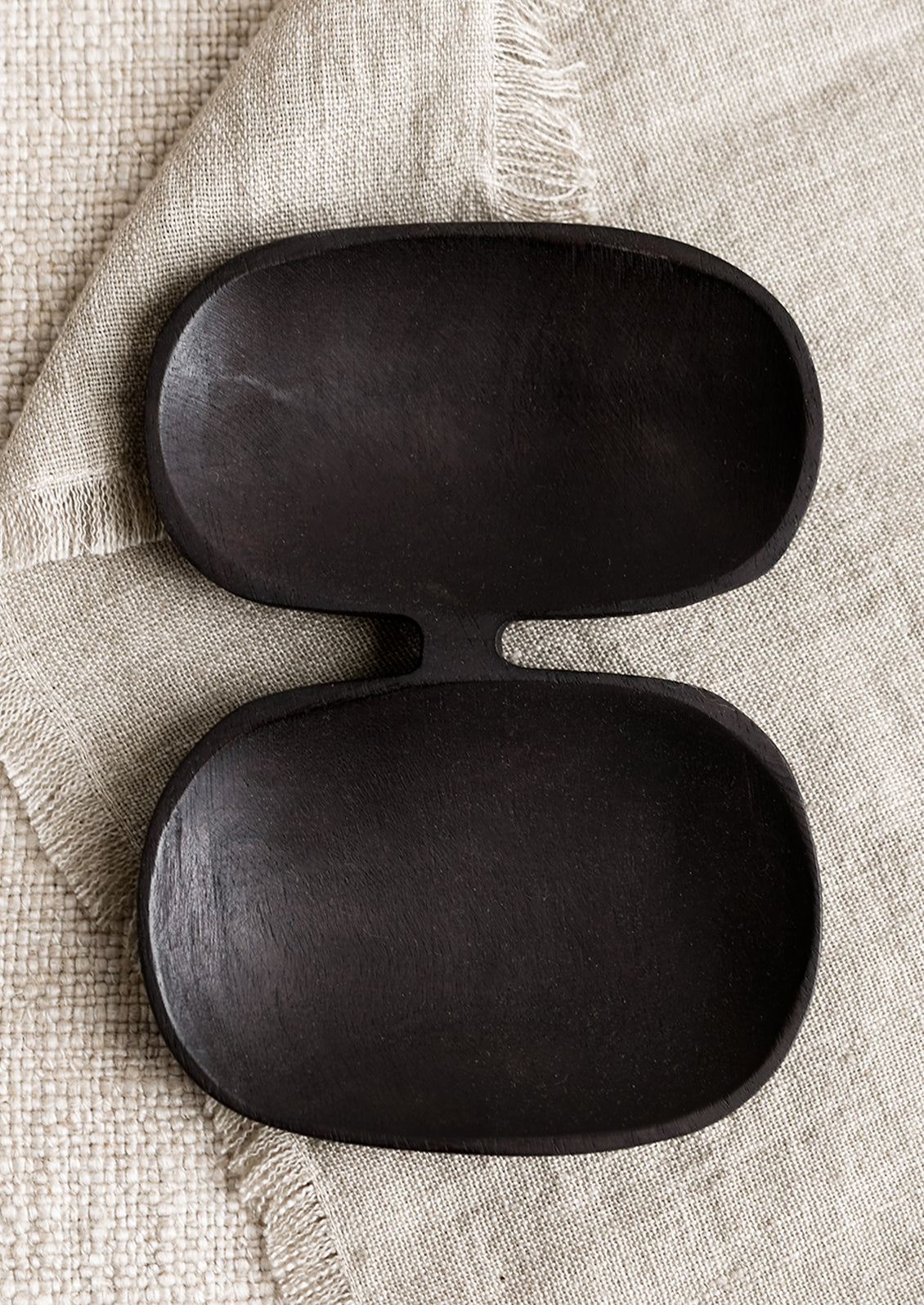 A double wide wooden dish with mirrored oval shape in blackened wood.