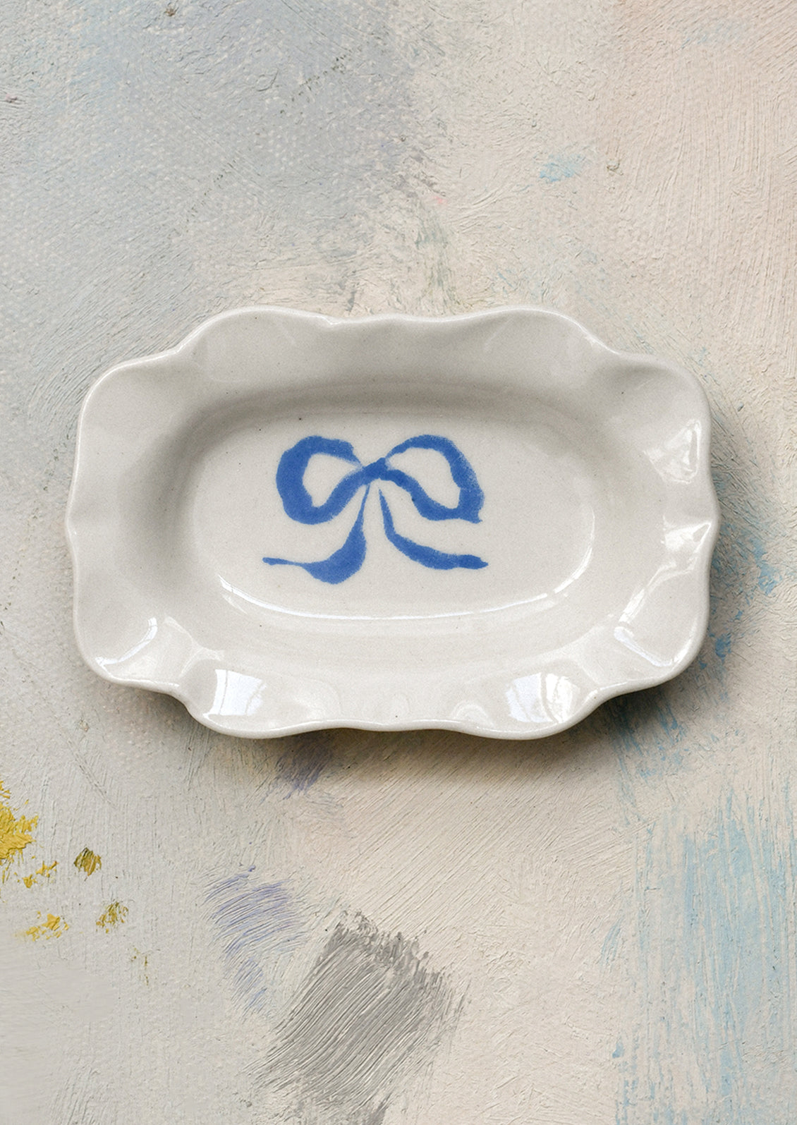 A small porcelain dish with ornate shape and hand painted bow illustration in blue.