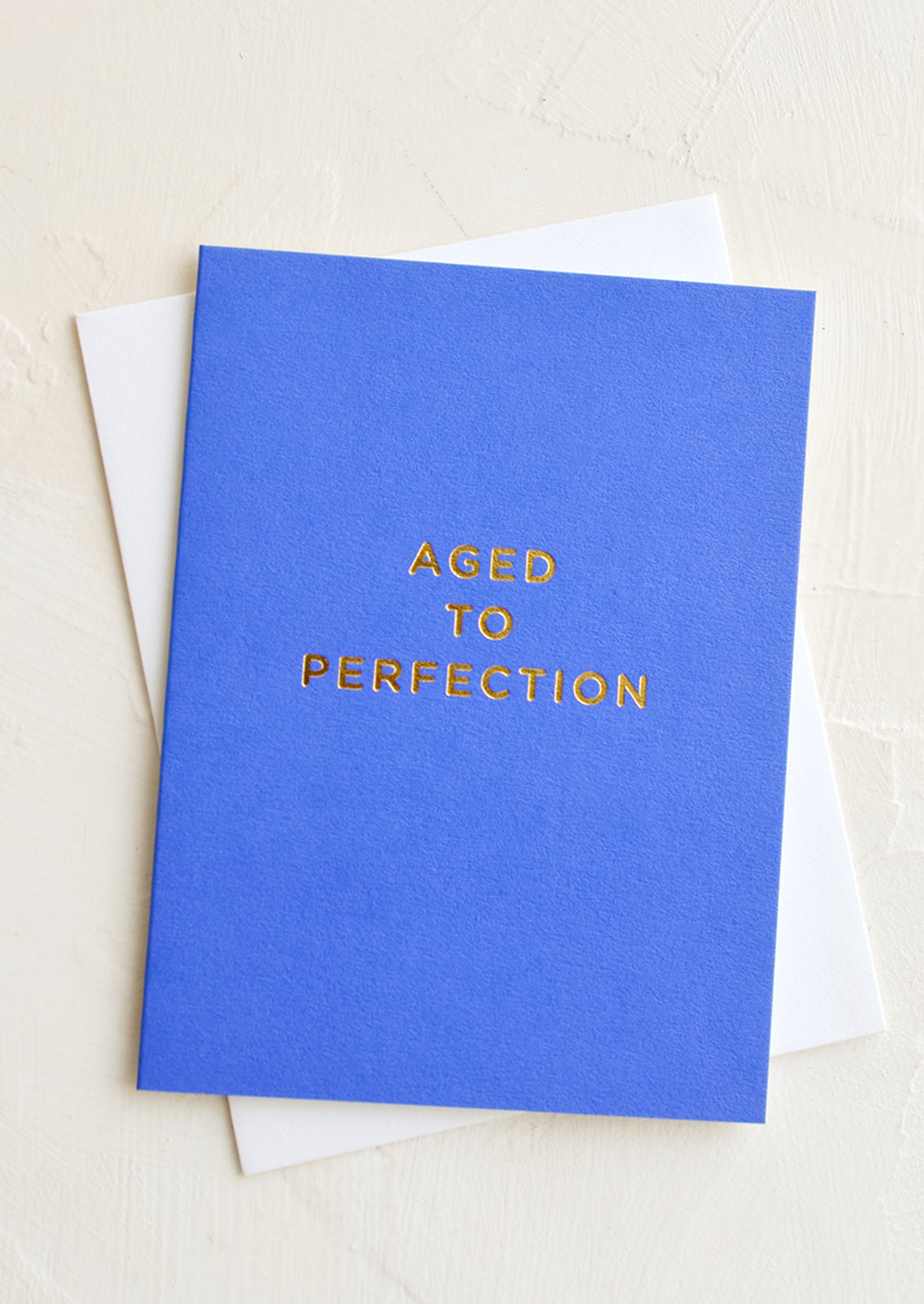A cobalt blue greeting card with golden lettering reading "Aged to perfection".