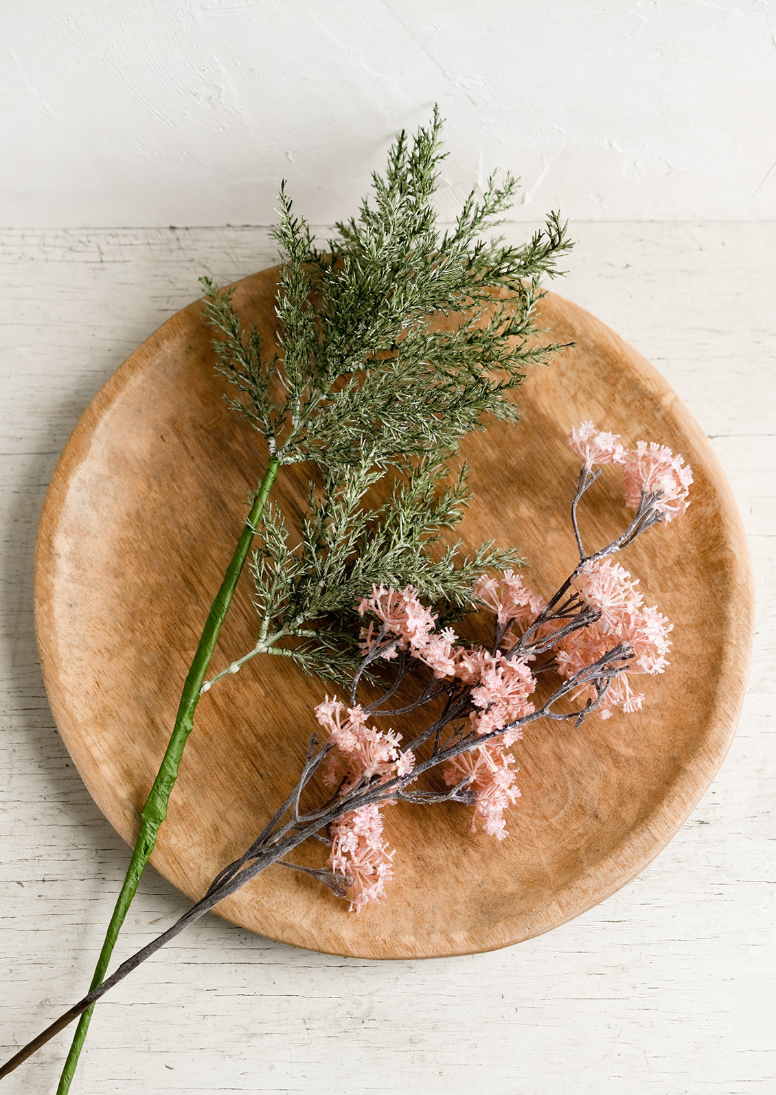 A round hardwood platter with faux flowers.