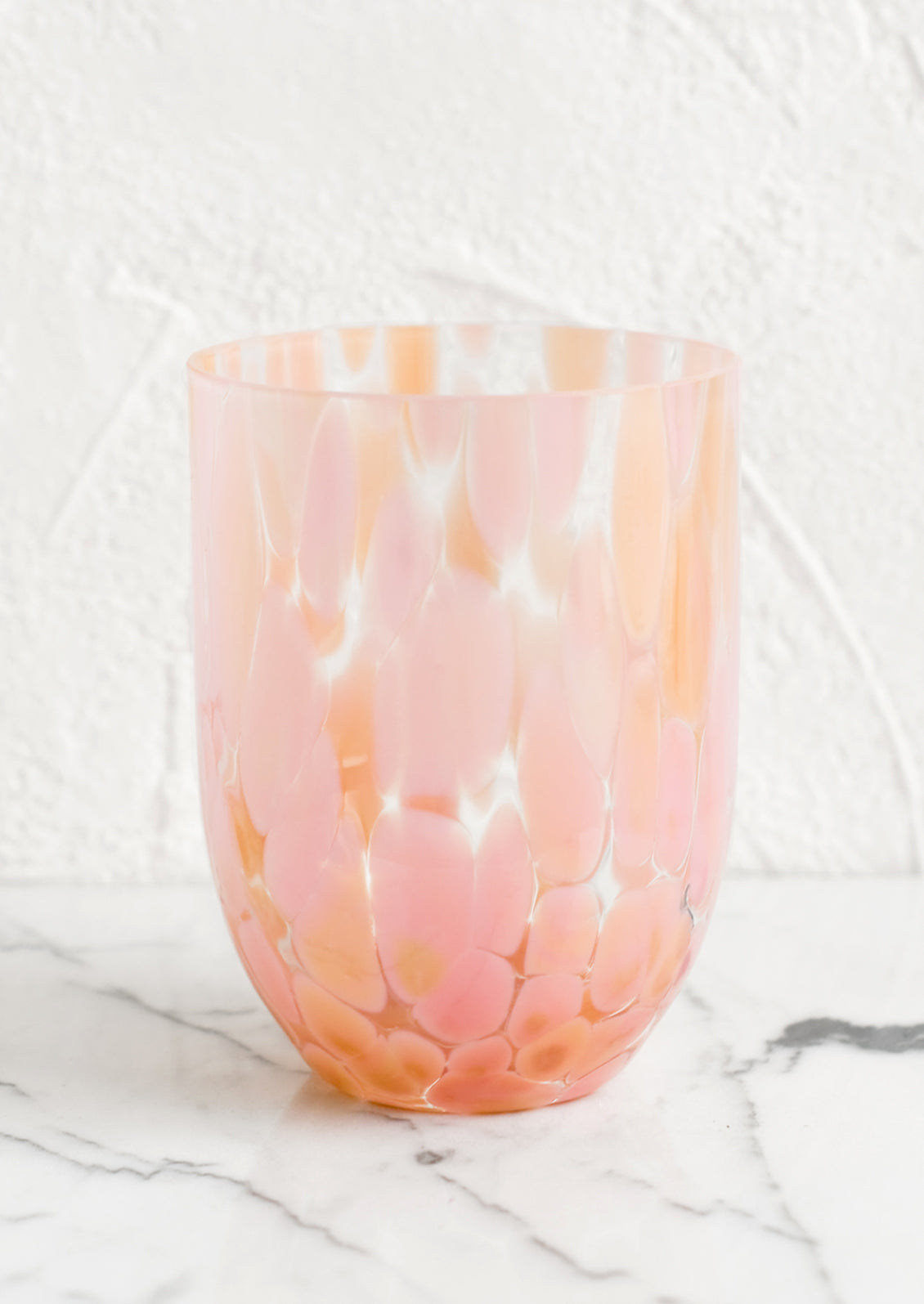 A handmade speckled glass juice cup with peach and pink spots.