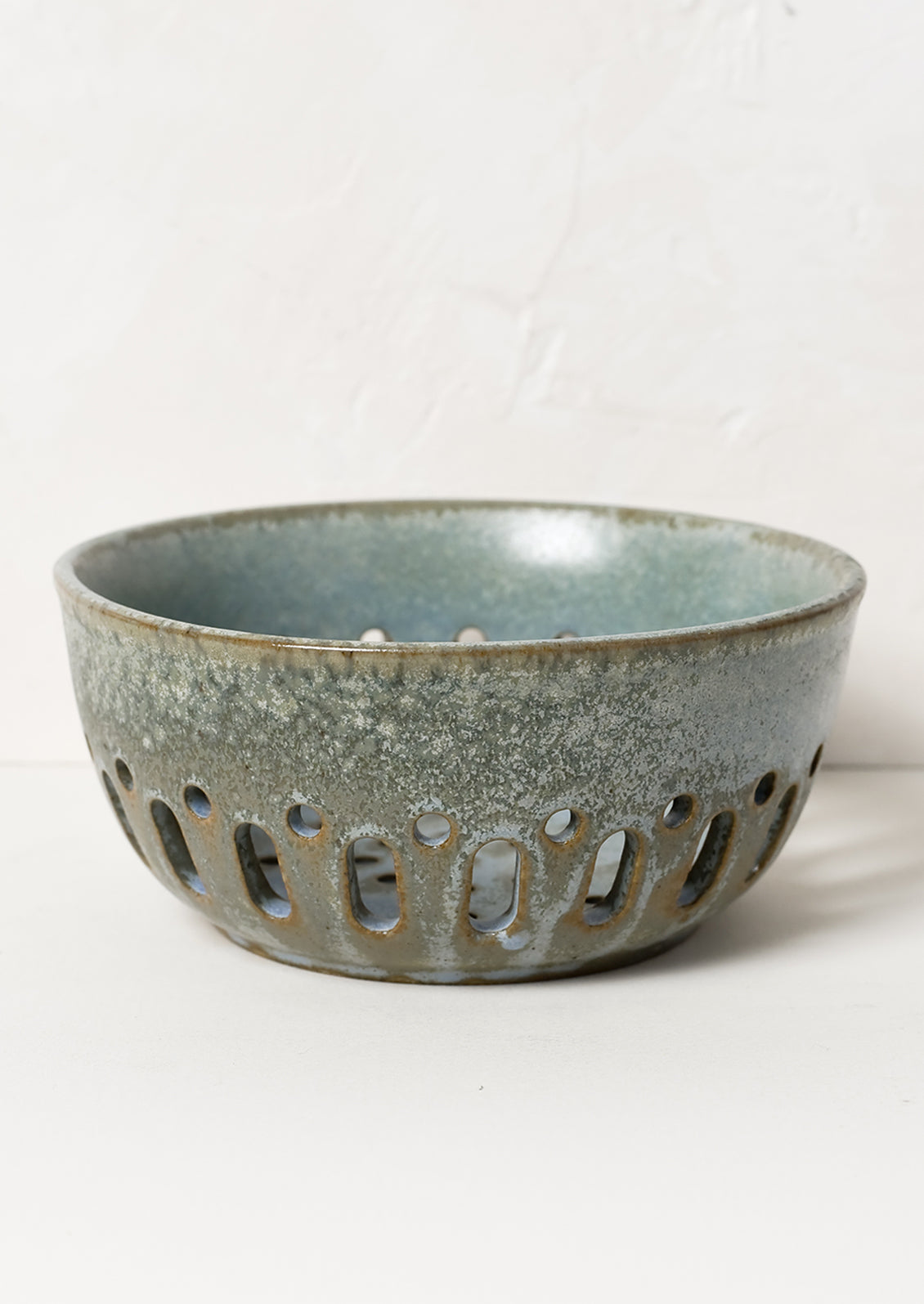 A ceramic berry colander in mottled blue green glaze.