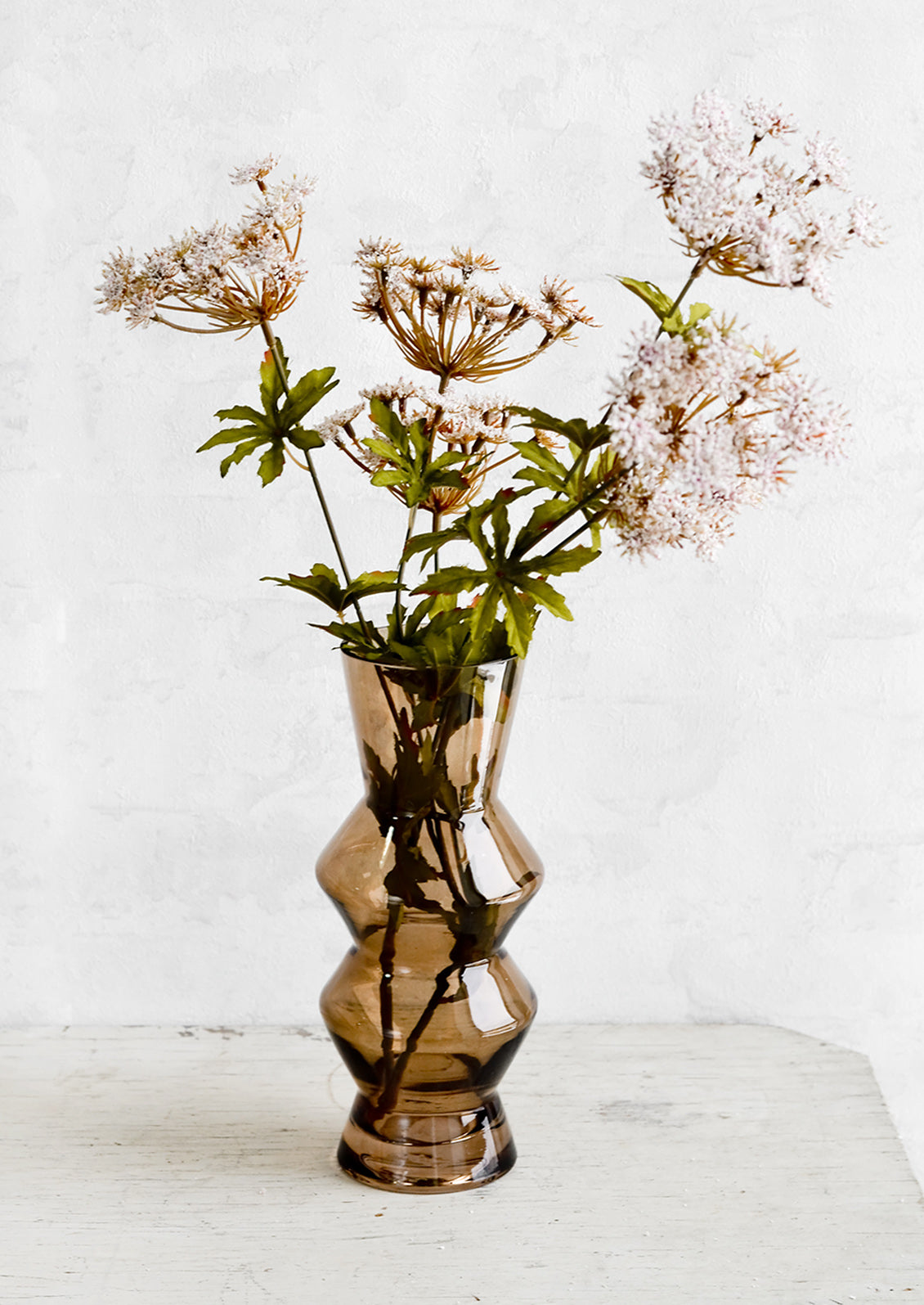 A brown glass vase holding tall flowers resembling Queen Anne's Lace.