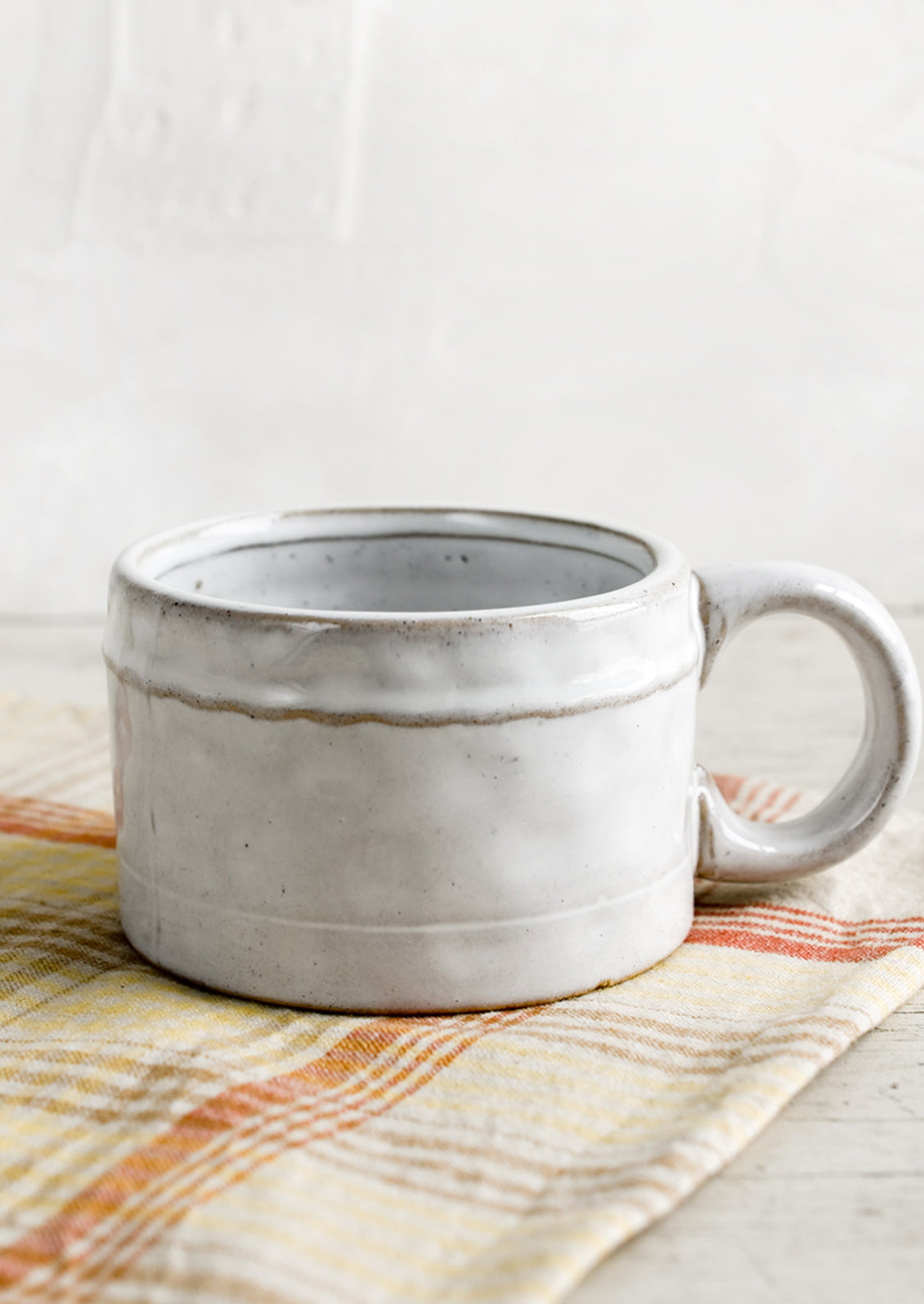 A ceramic mug in glossy white glaze with single wavy line detail.