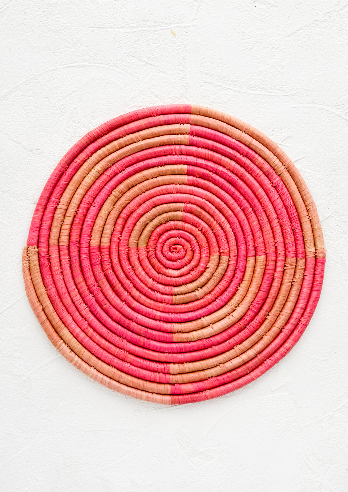 A round trivet made from woven raffia in two shades of pink.