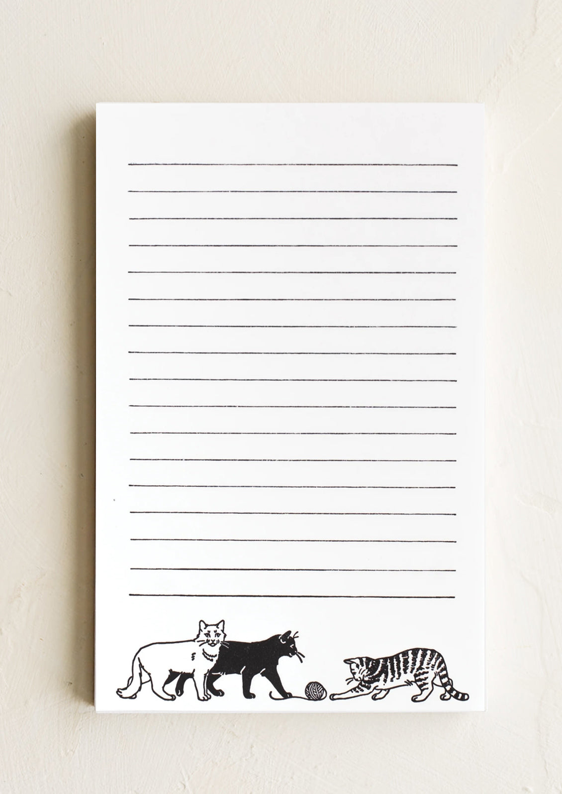 A white notepad with black lines and cat print with yarn.