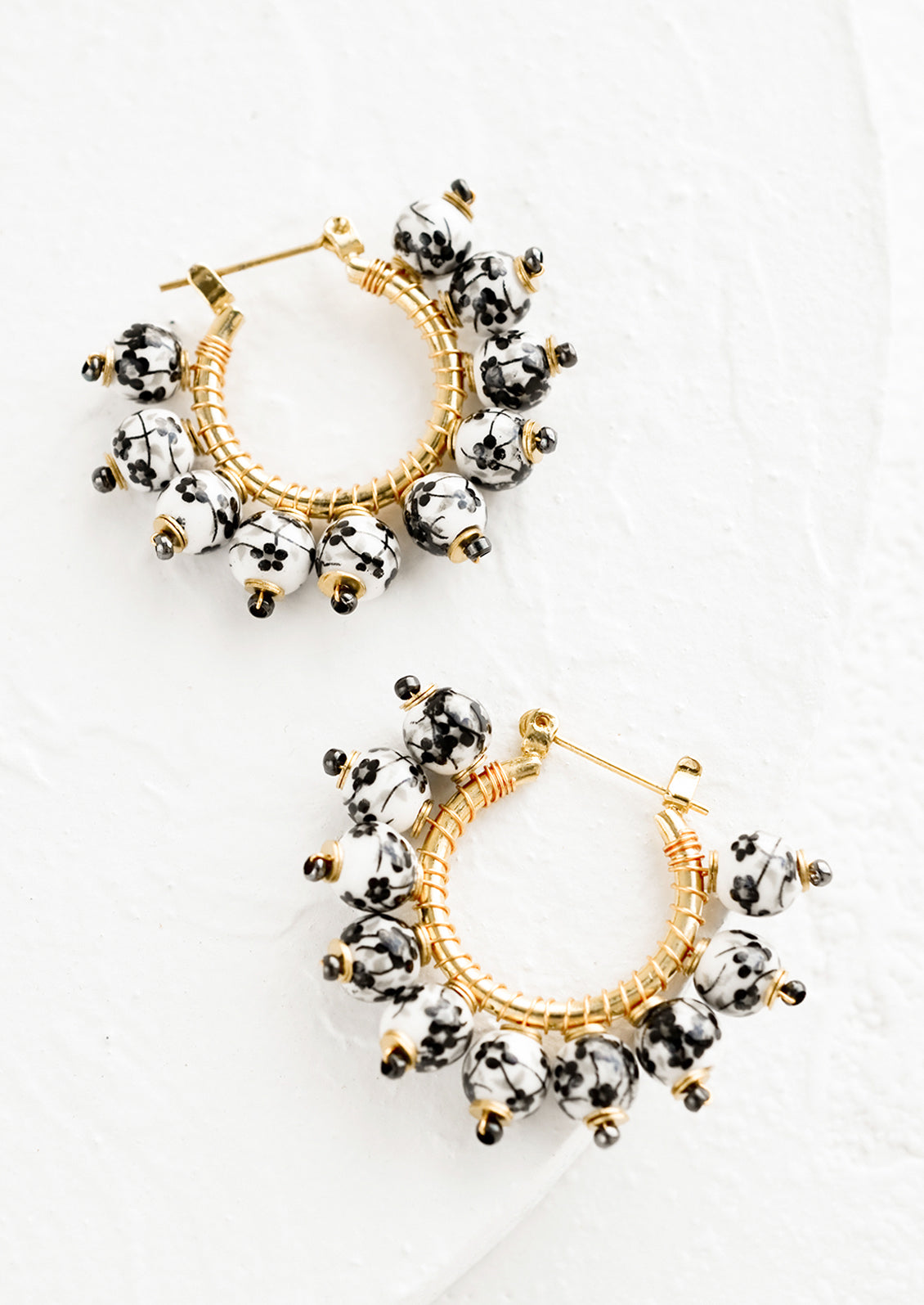 A pair of gold hoop earrings with black and white chinoiserie floral beads.