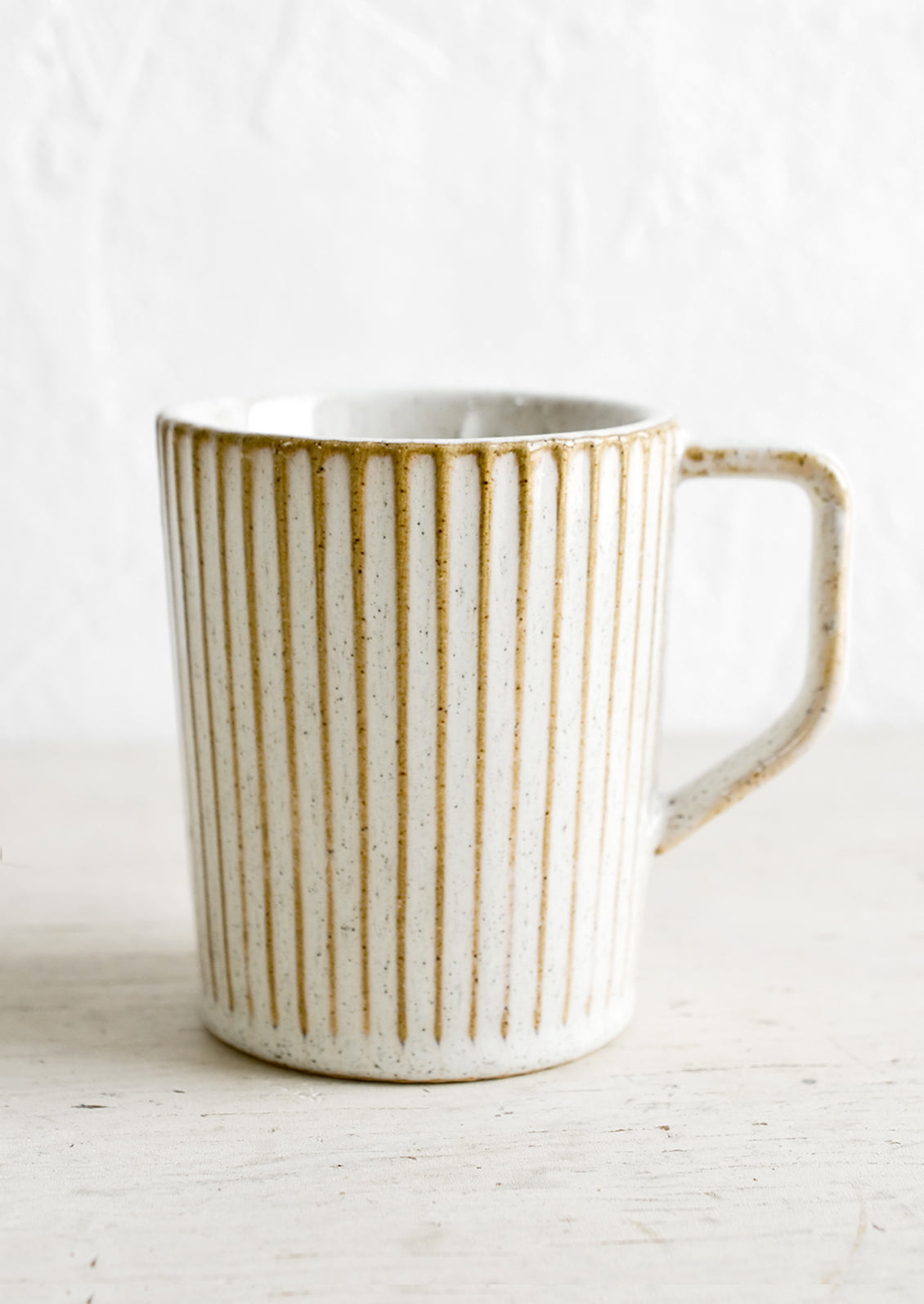 A ceramic mug with a handle in a glossy, neutral tan glaze with vertical grooved texture.