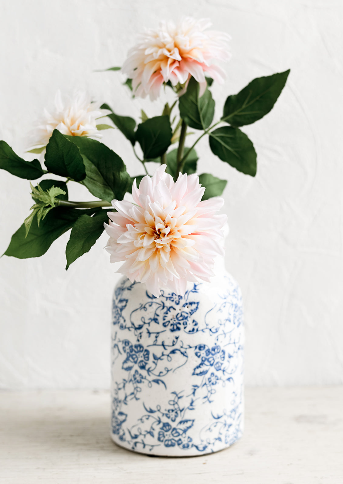A blue and white ceramic vase with antique floral print, holding dahlias.