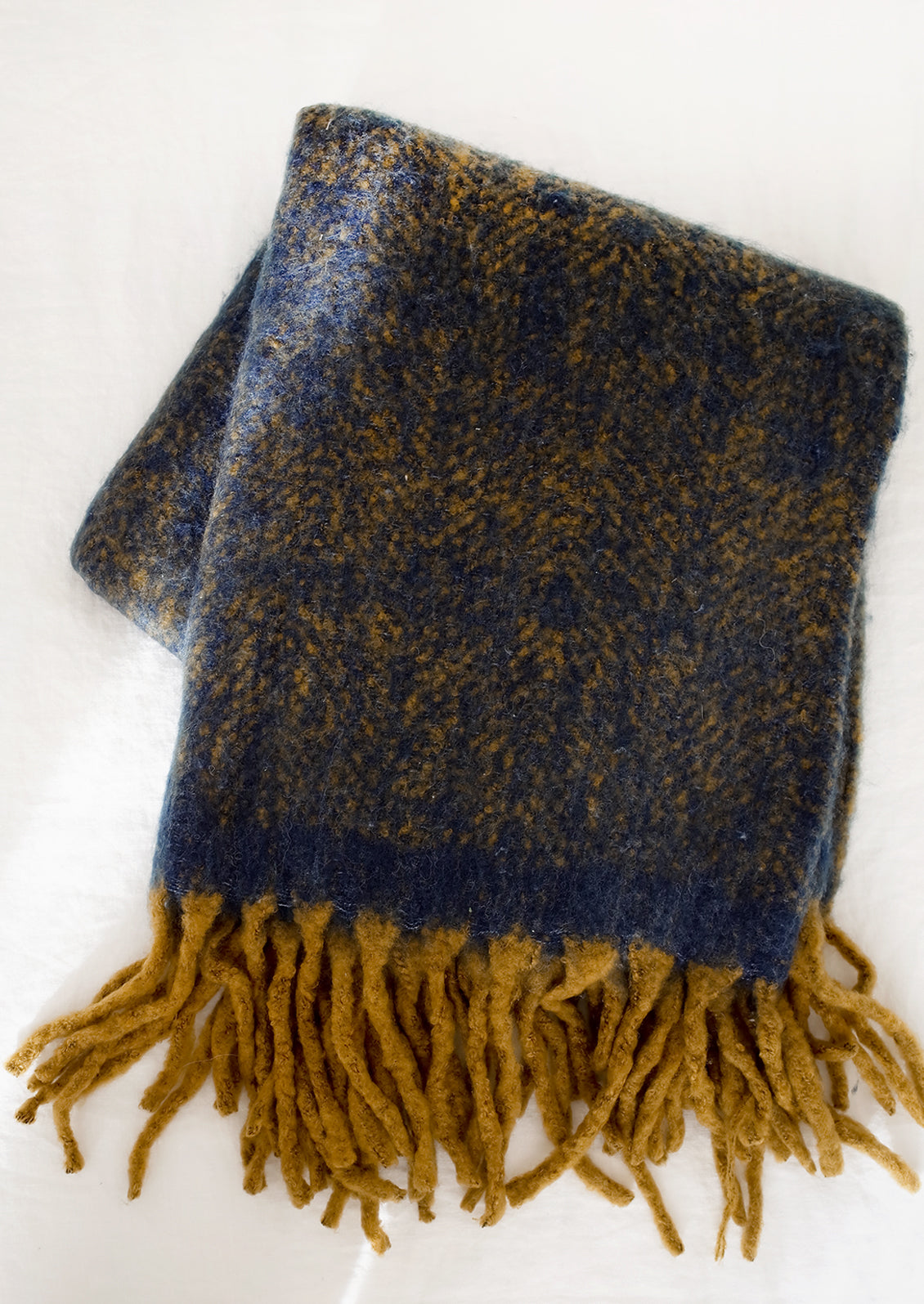 A fuzzy mohair-like blanket in navy and mustard with mustard tassel trim.