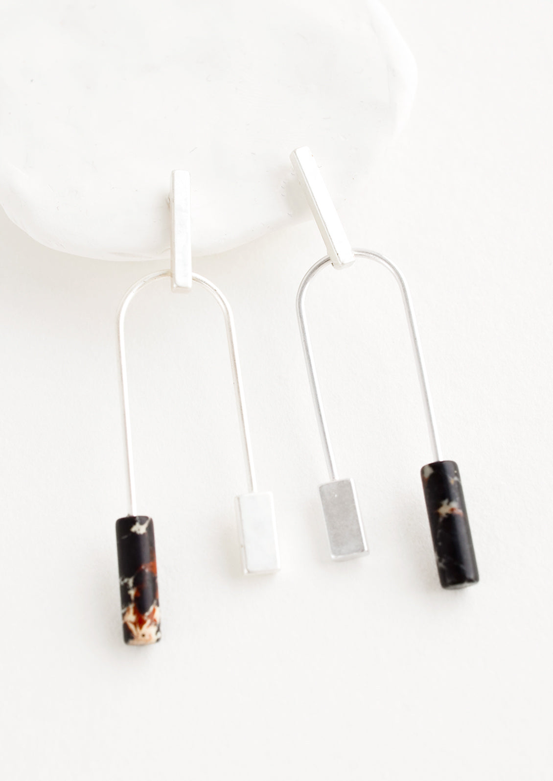 A pair of silver earrings with bar shaped top and arched bottom with black gemstone on one side.