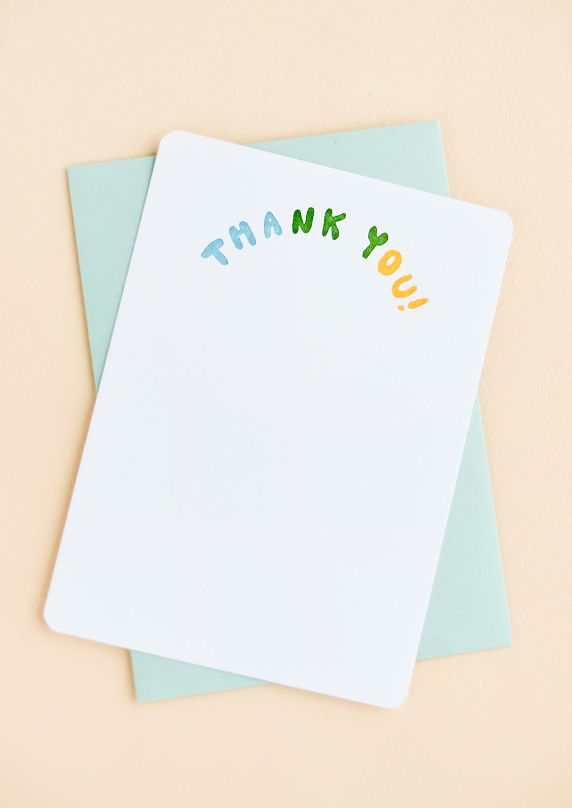 A white notecard with "Thank you" in colorblocked, arc-shaped text at top, paired with a turquoise envelope.