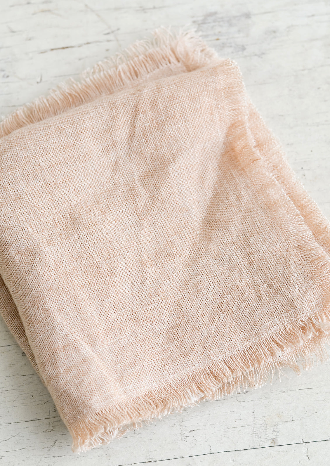 A folded dusty pink linen napkin with frayed edges.