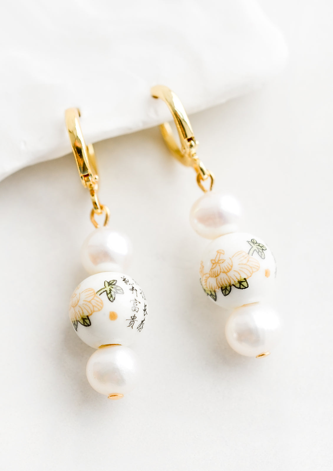 A pair of pearl earrings with gold huggie hoop clasp and Chinese ceramic beads.