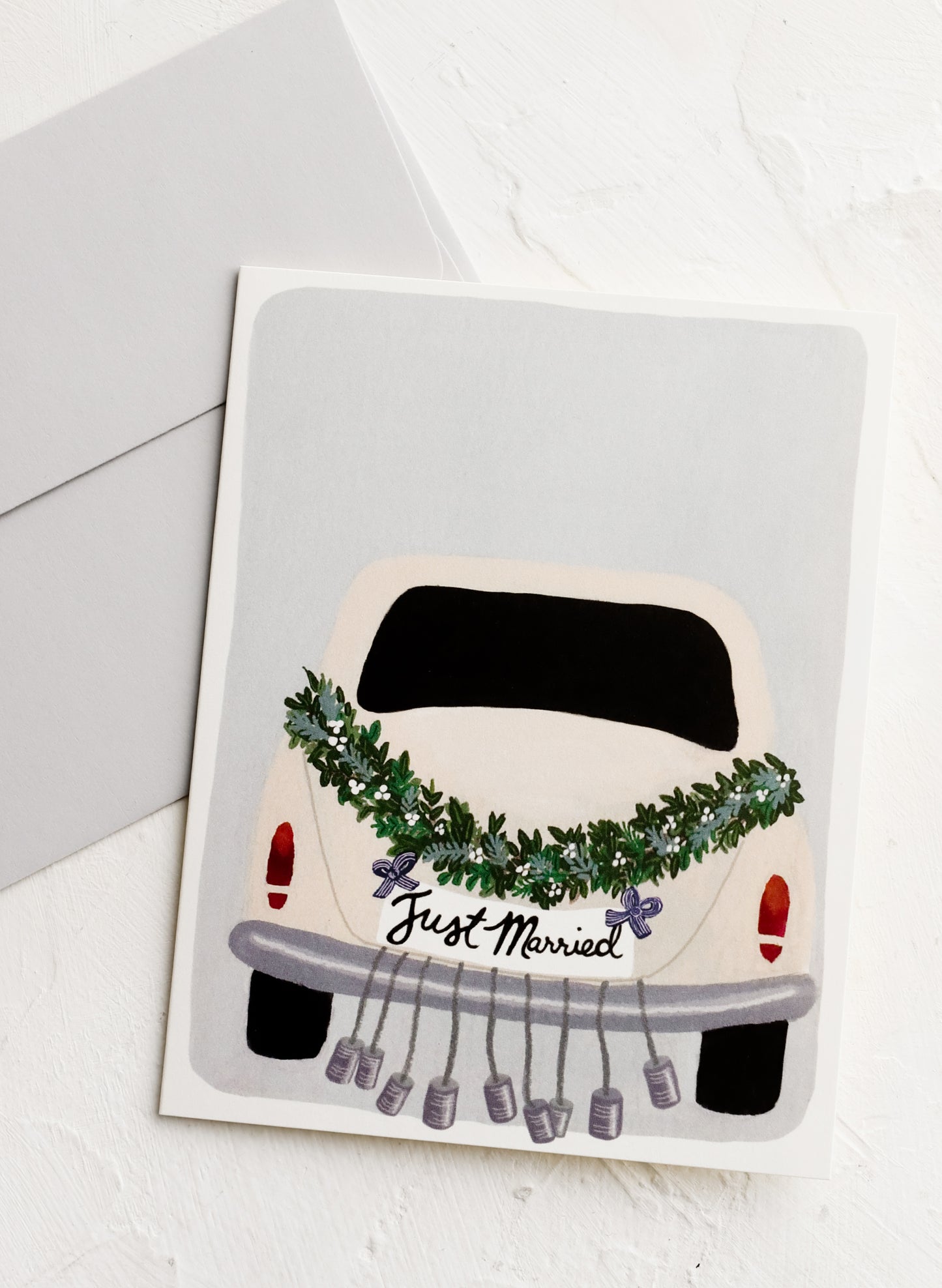 A greeting card with illustration of a car dressed up with "just married" bells.