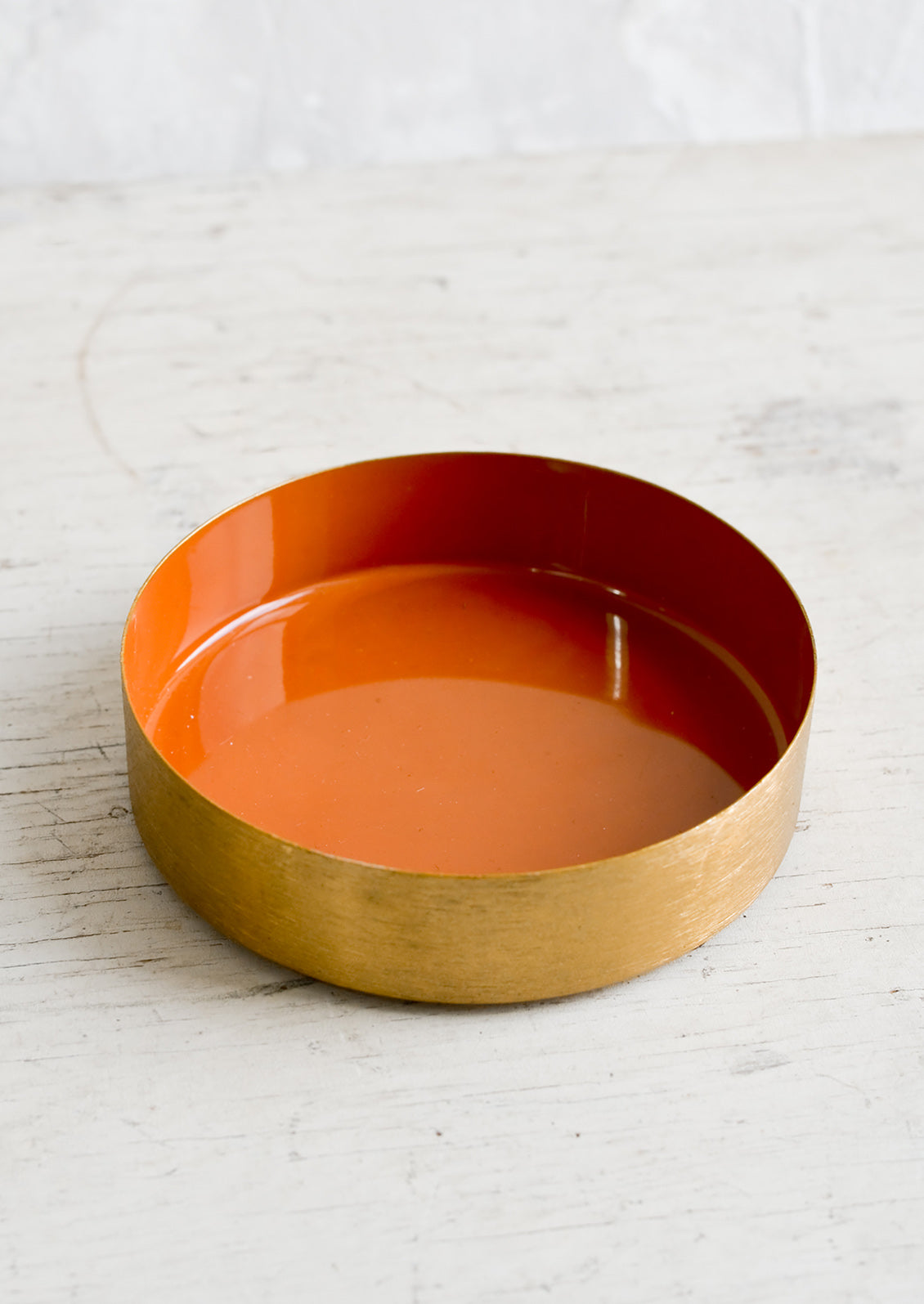 A small, round enamel tray with shallow brass rim and terracotta interior.