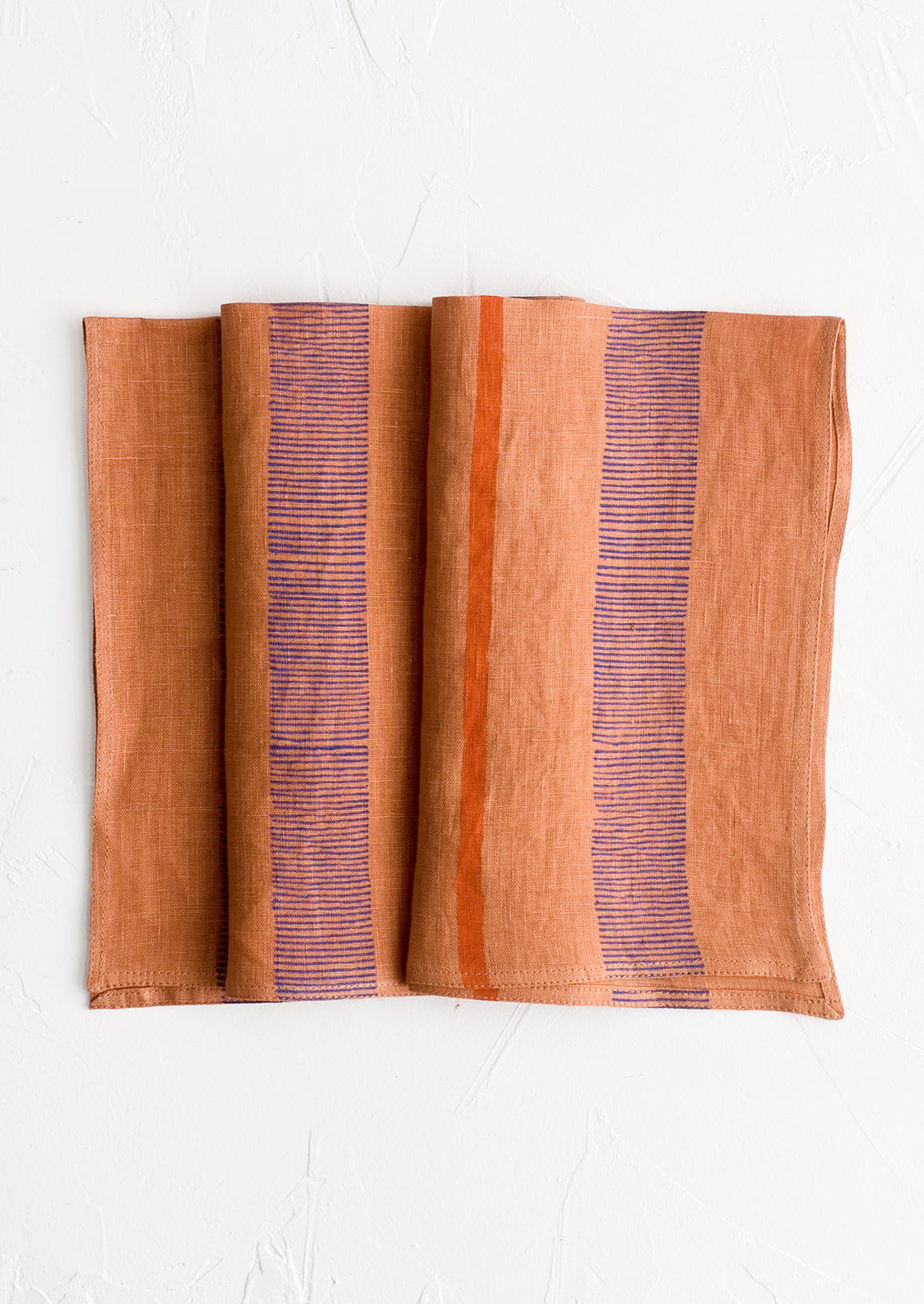 A terracotta linen napkin with block printed stripe design.