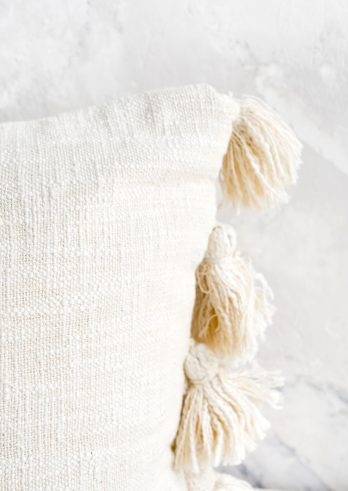 Textured cotton pillow with tonal, decorative tassels at side.