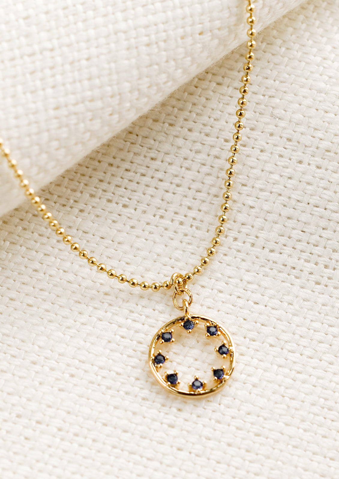 A gold necklace with circular pendant with blue inner stones.