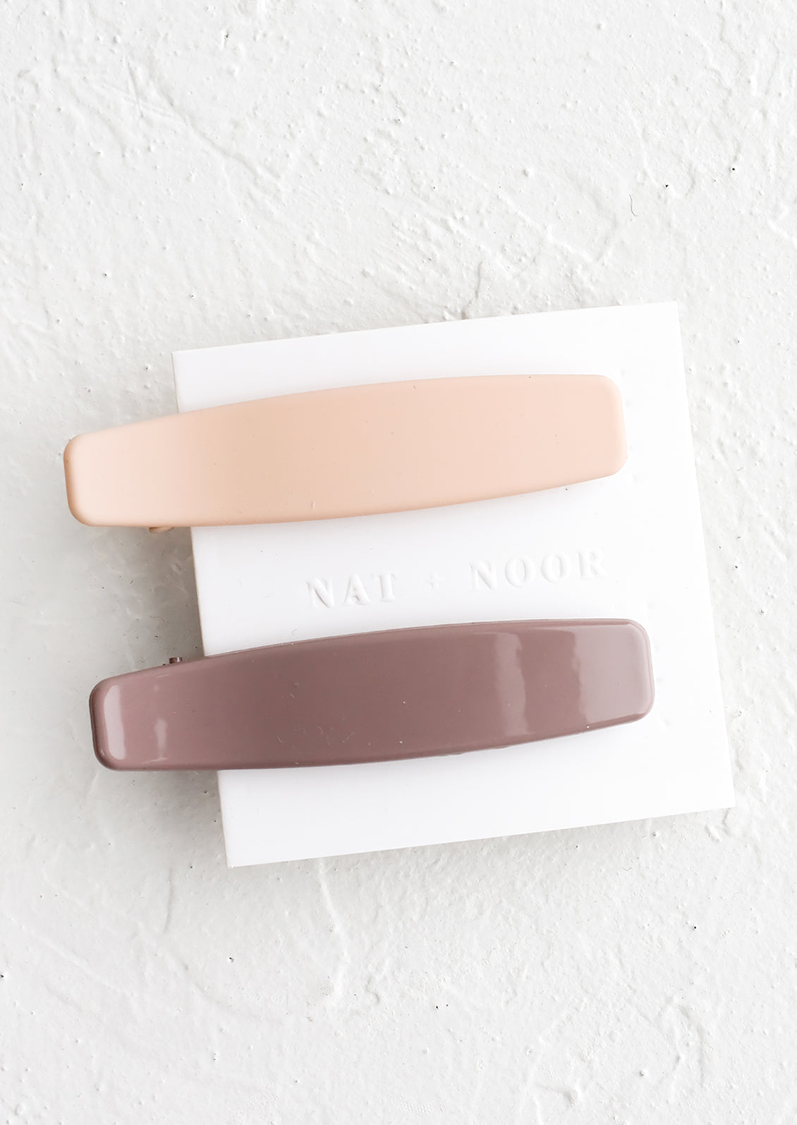 A pair of hair clips with one nude and one mauve.