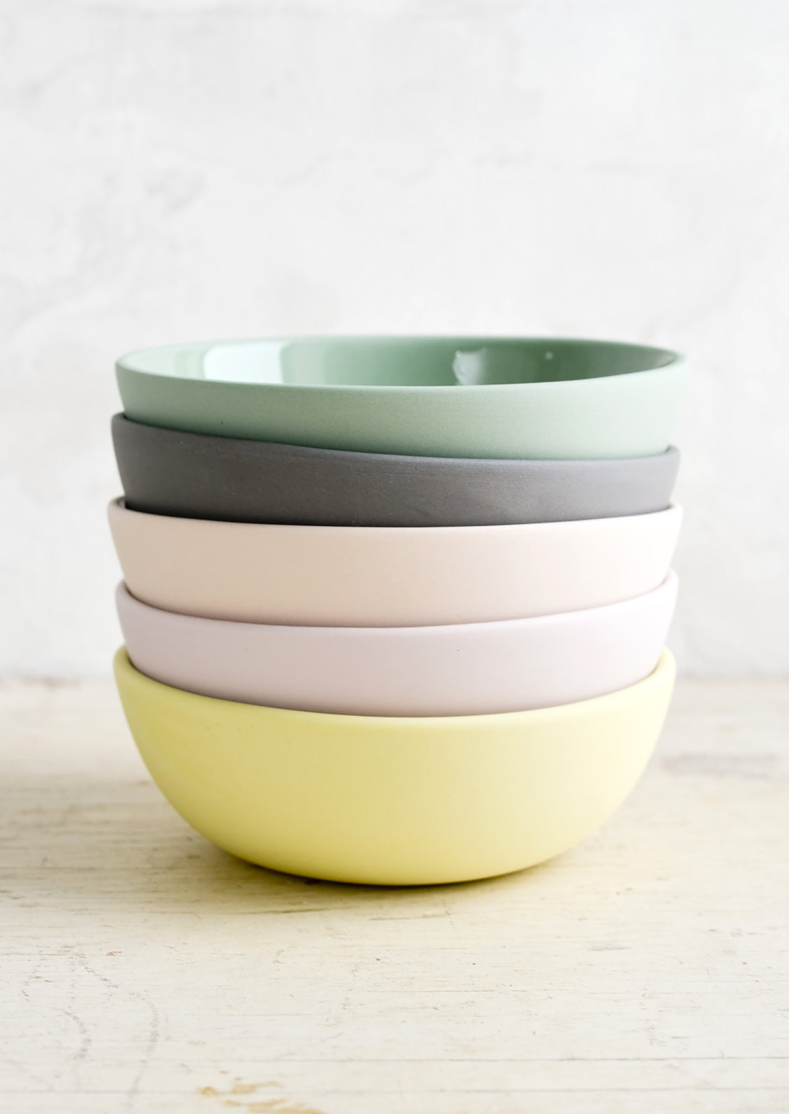 A stack of bowls with matte exterior and glossy interior in assorted pastel hues.