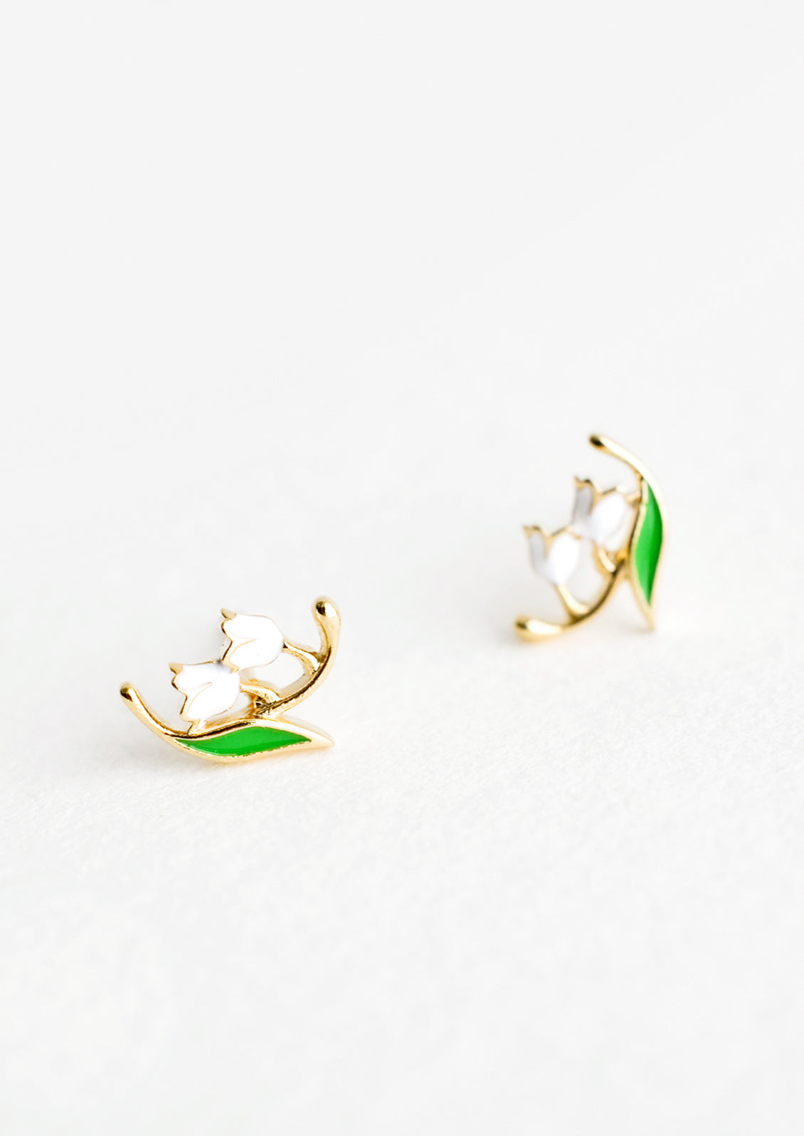 Small gold stud earrings in the shape of a lily of the valley flower, constructed in green and white enamel finish.