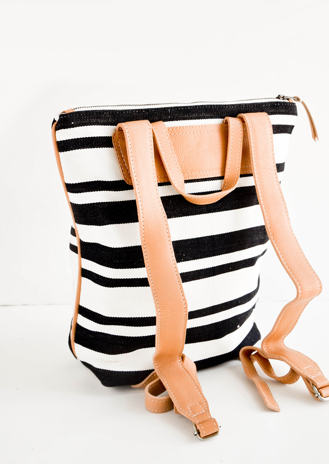 Tanned leather straps on the back of black & white striped canvas backpack