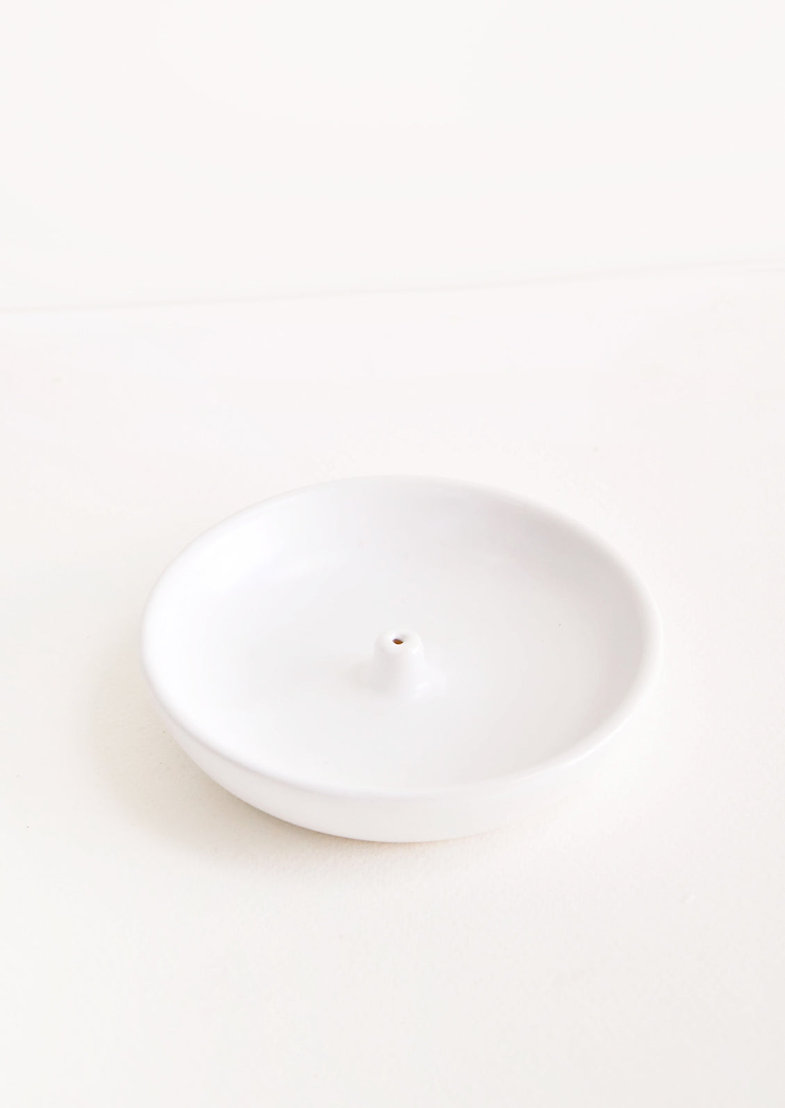 A simple white dish with a small hold at the center for holding incense.