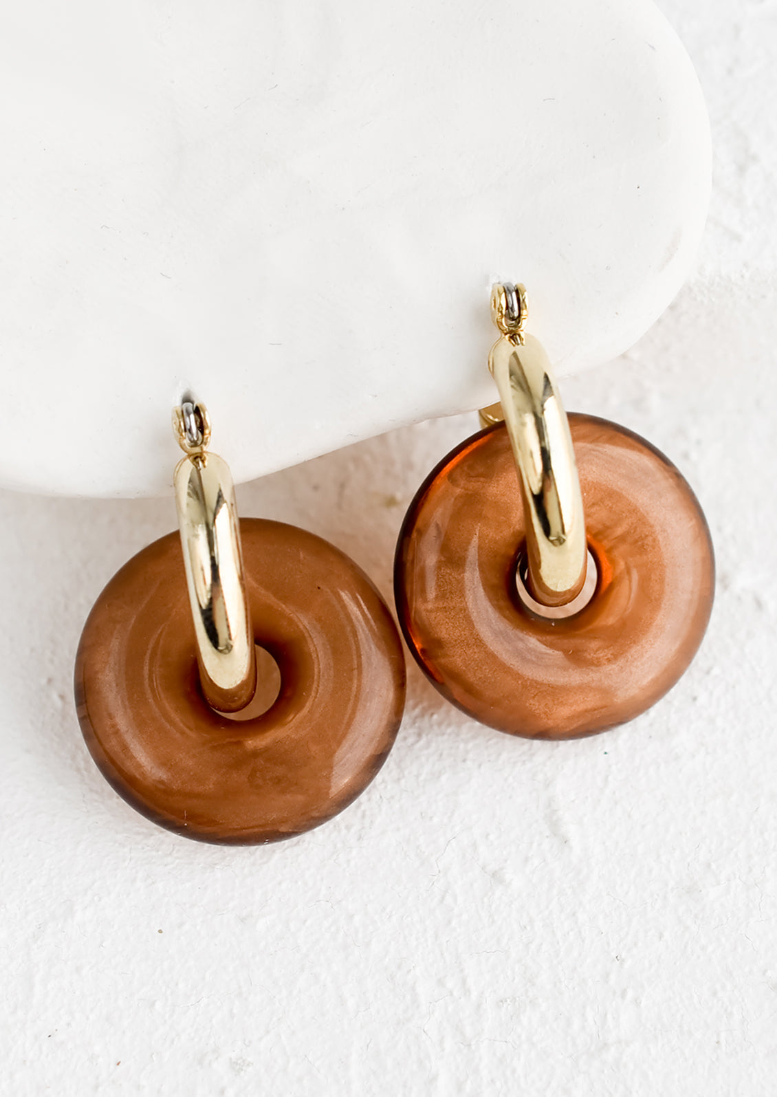 A pair of brown resin donut shaped charms on gold hoop earrings.