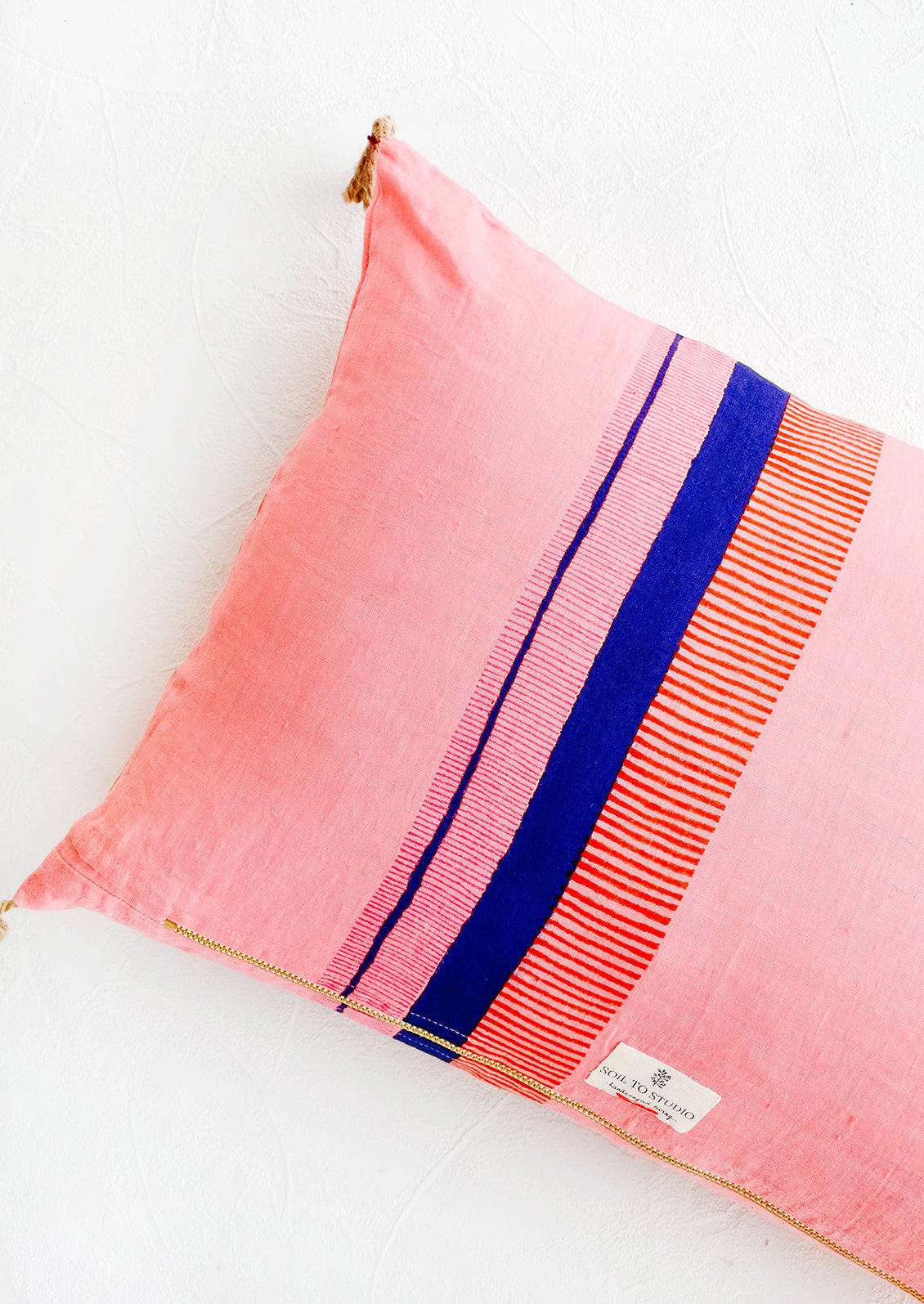 Backside of decorative pink linen throw pillow, block printed stripe detail and exposed metal zipper