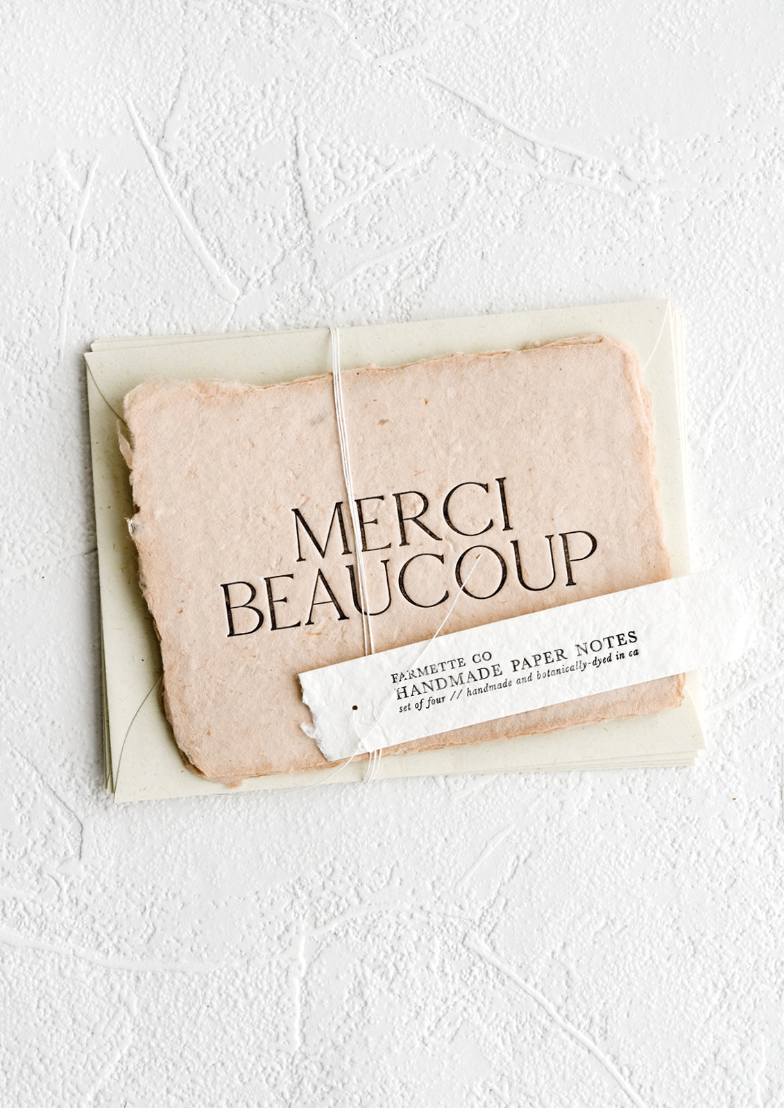 A pack of greeting cards made from blush handmade paper and large letters spelling "Merci Beaucoup".