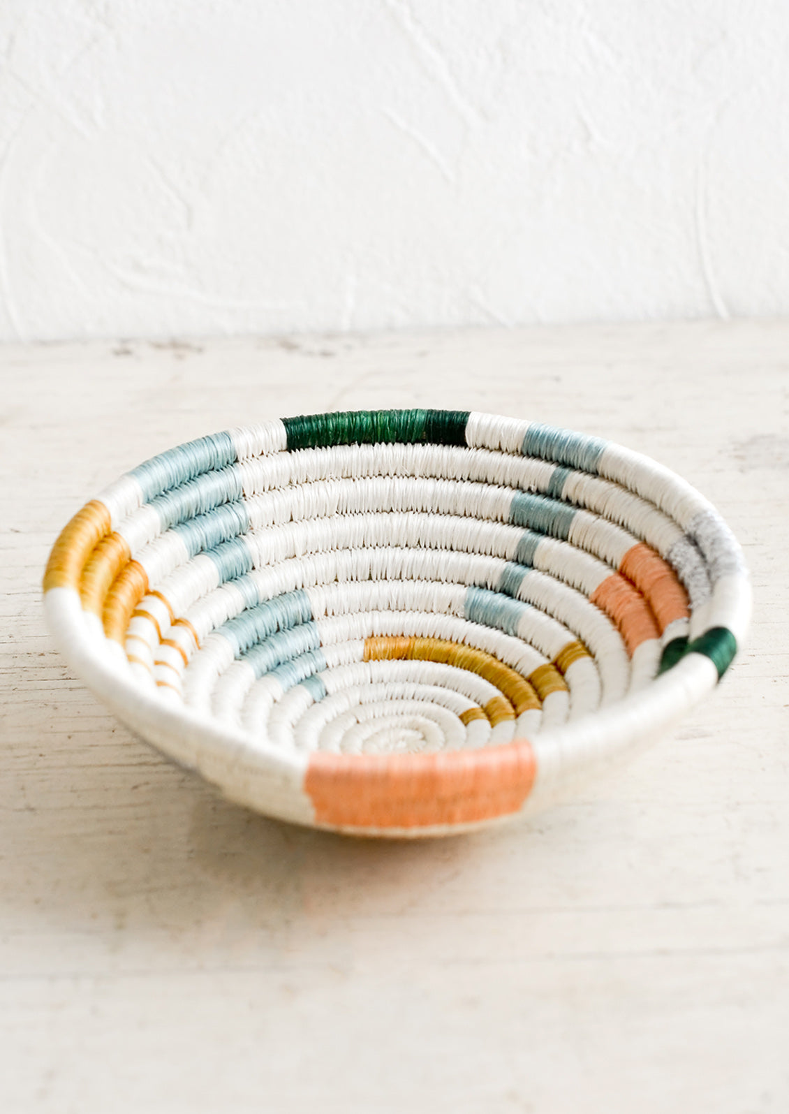 A small catchall bowl made from sweetgrass in pastel colored geometric pattern.