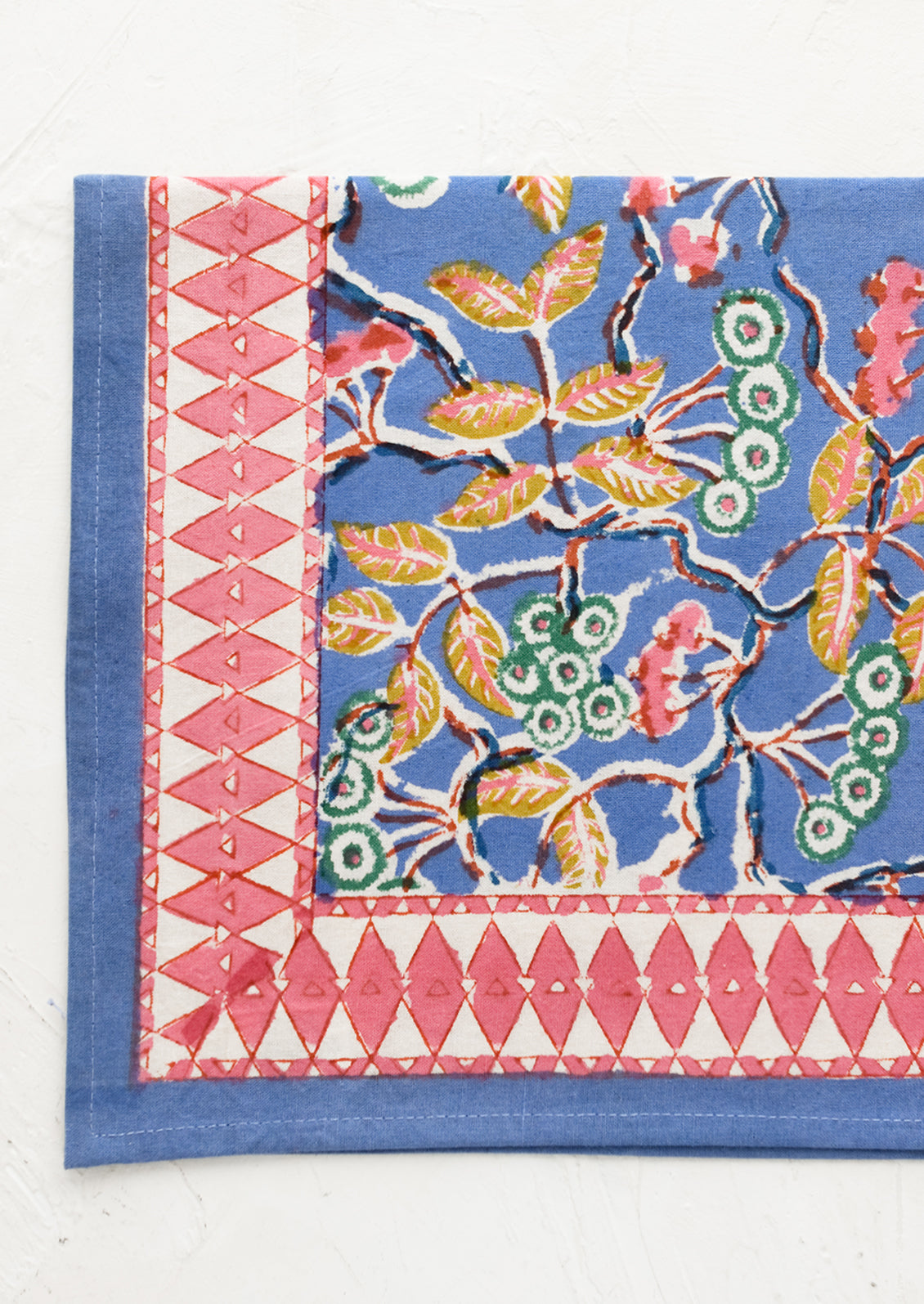 A folded cotton napkin in blue botanical print with pink geometric border.