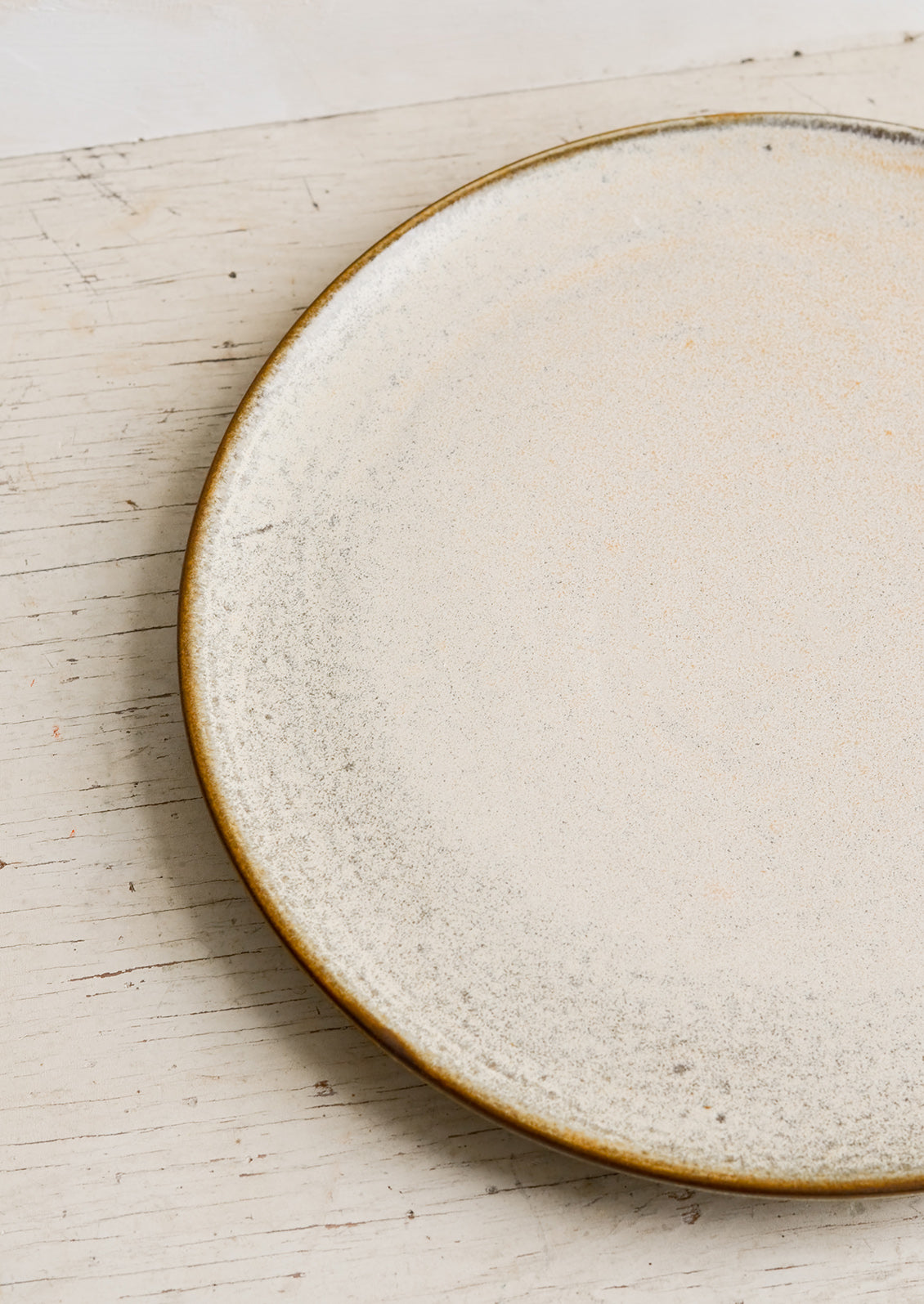 A round ceramic plate in matte cream glaze with subtle speckled texture.