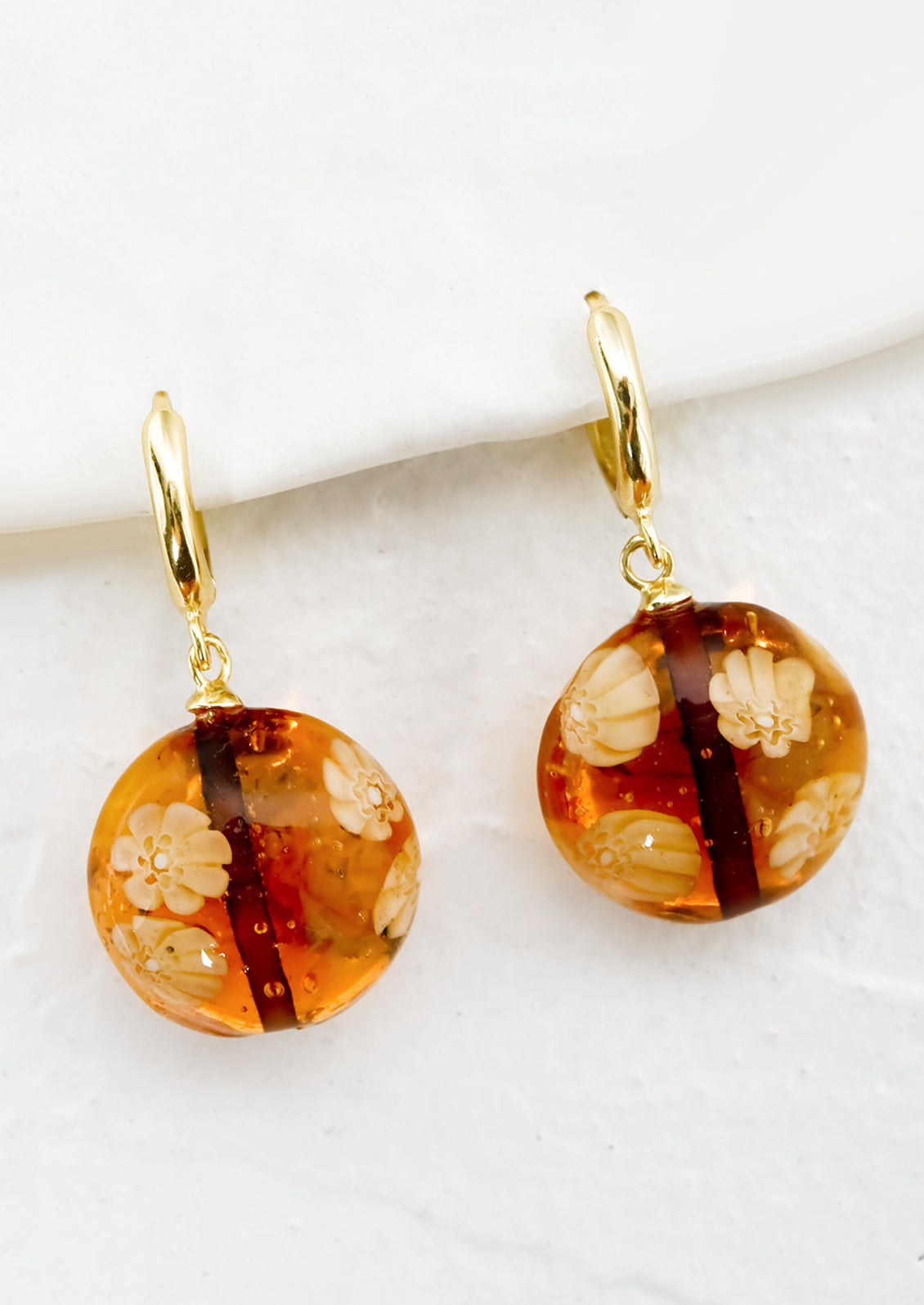 A pair of gold huggie hoops with sepia murano glass beads.