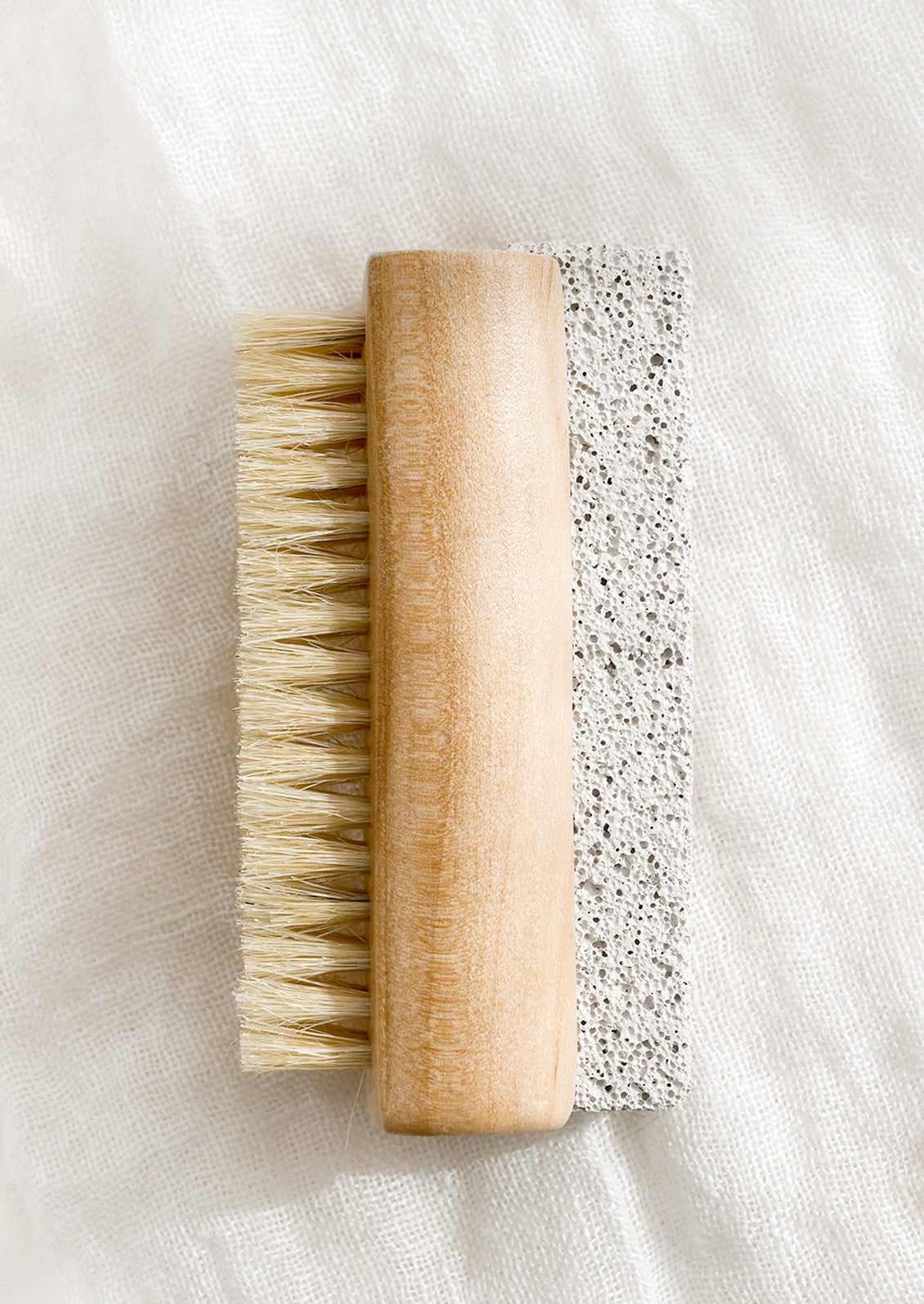 A light wood nail brush with brush on one side and pumice stone on the other.